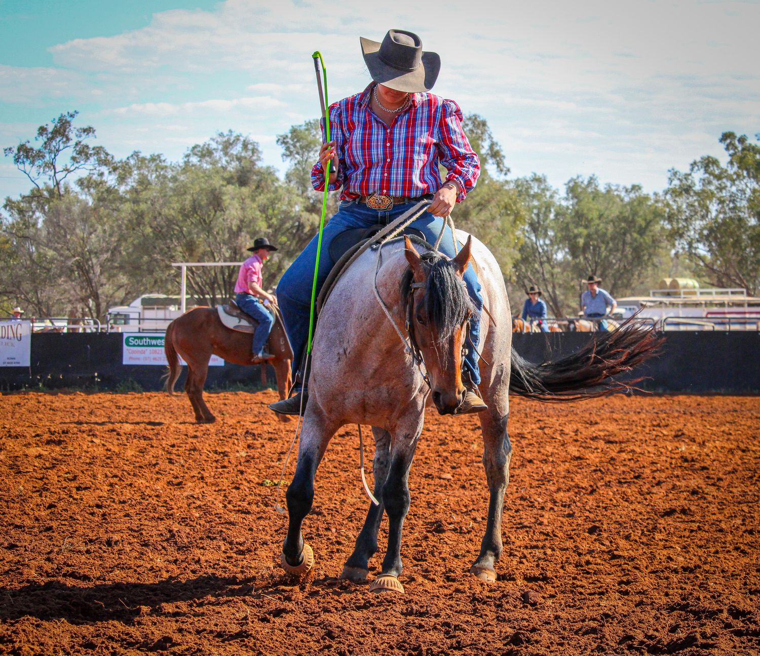 Western riders practicing horsemanship skills in a red dirt arena.