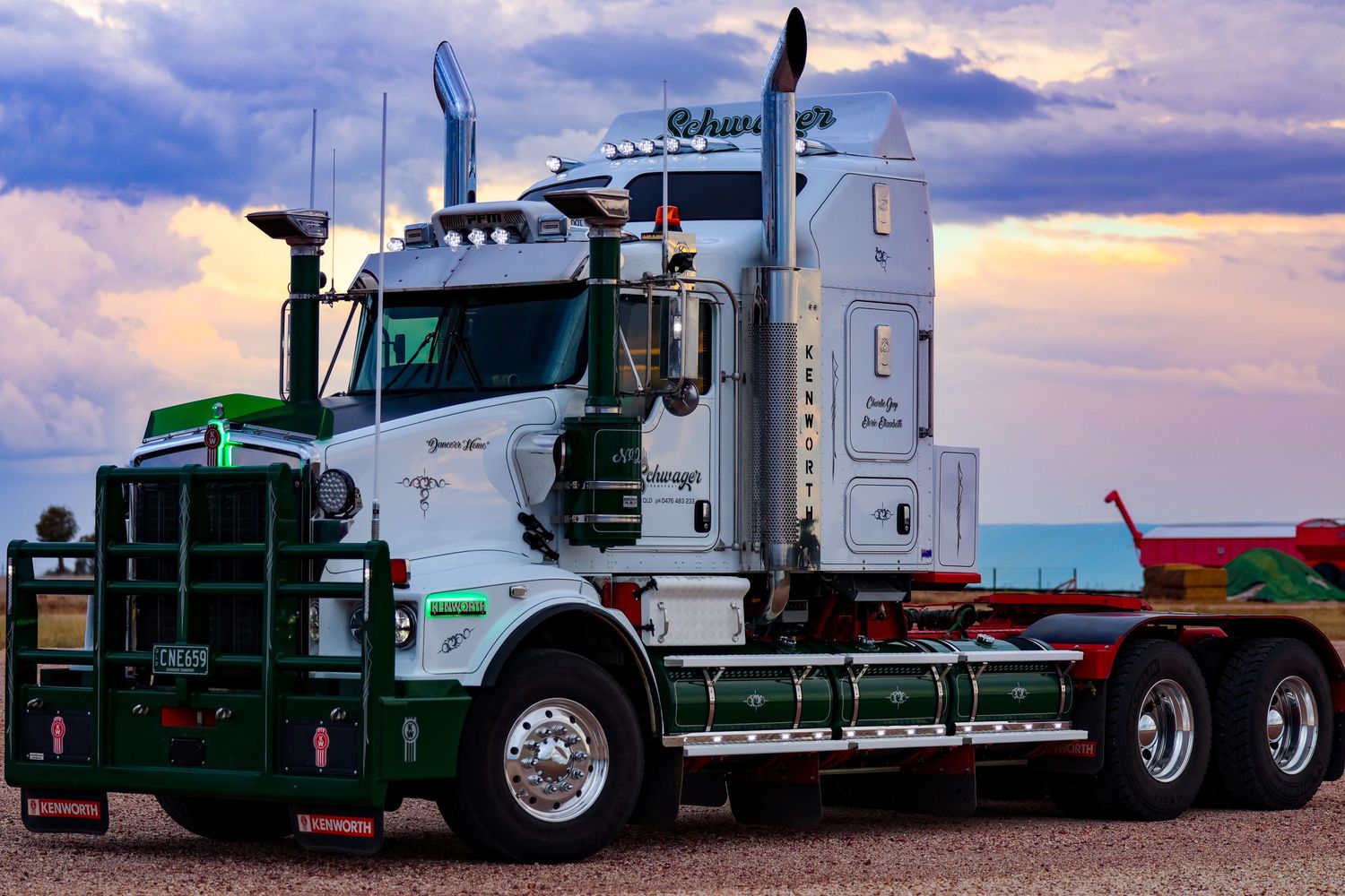 Side view of white and green semi trucks lined up against a dramatic cloudy sunset sky.