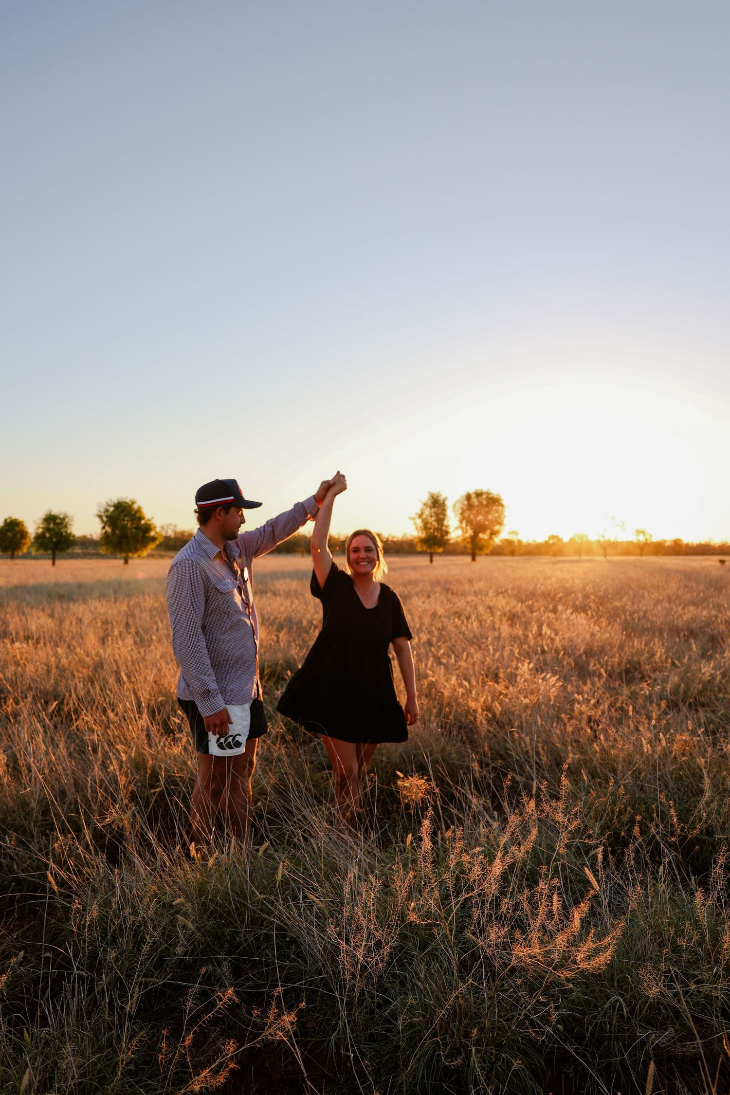 Two people walking through a golden wheat field at sunset with warm light illuminating the landscape.