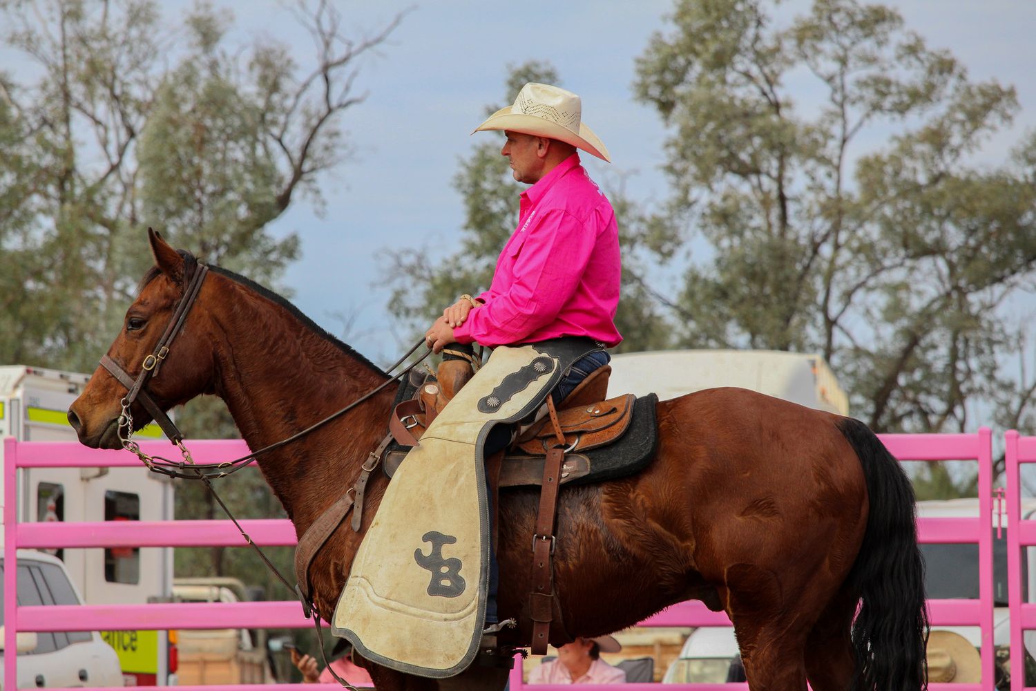 A rider in pink shirt and cowboy hat guides their horse over a pink-painted jump during an equestrian competition.