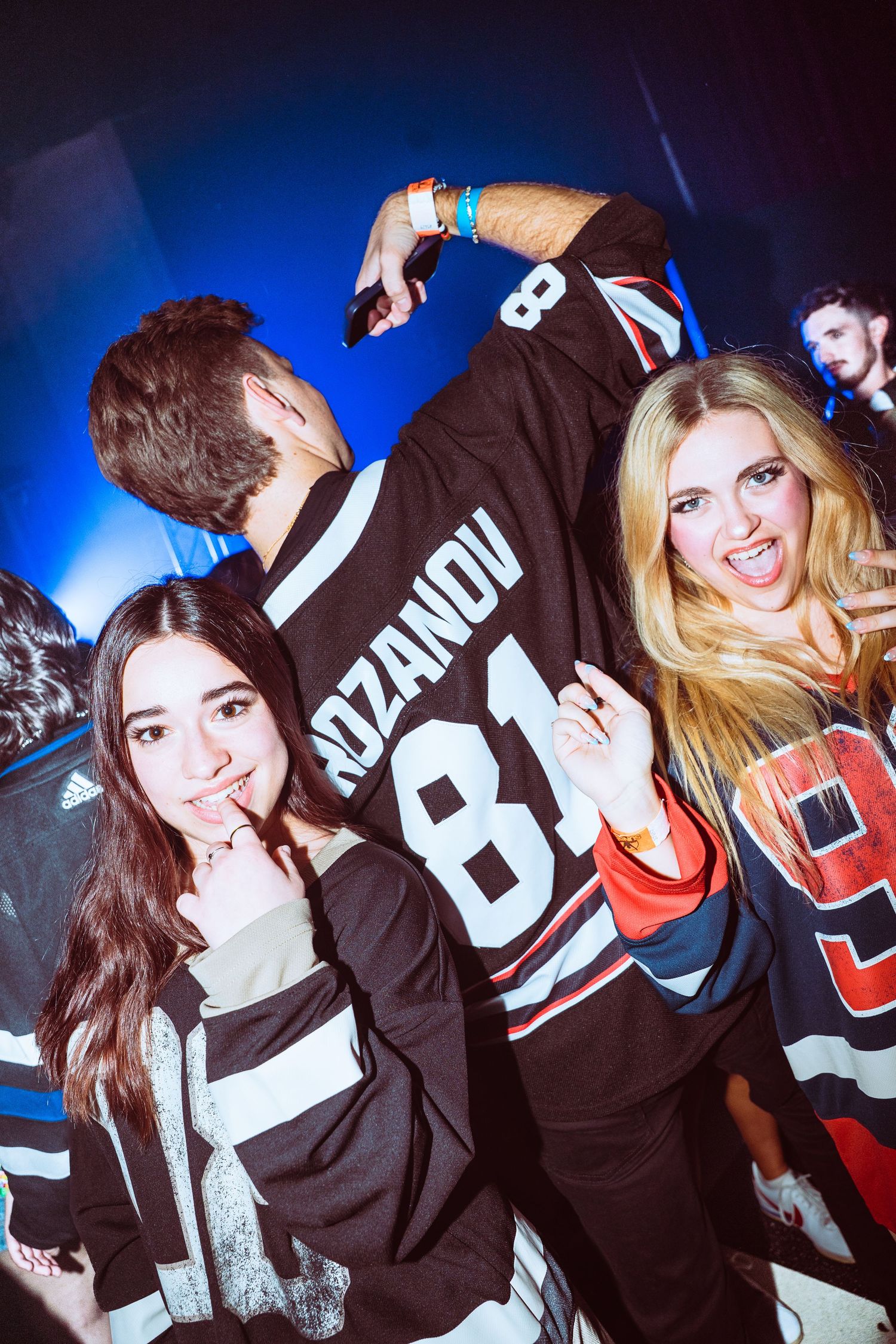 Three partygoers dance at a nightclub, two wearing hockey jerseys including a Rozanov 81 jersey.