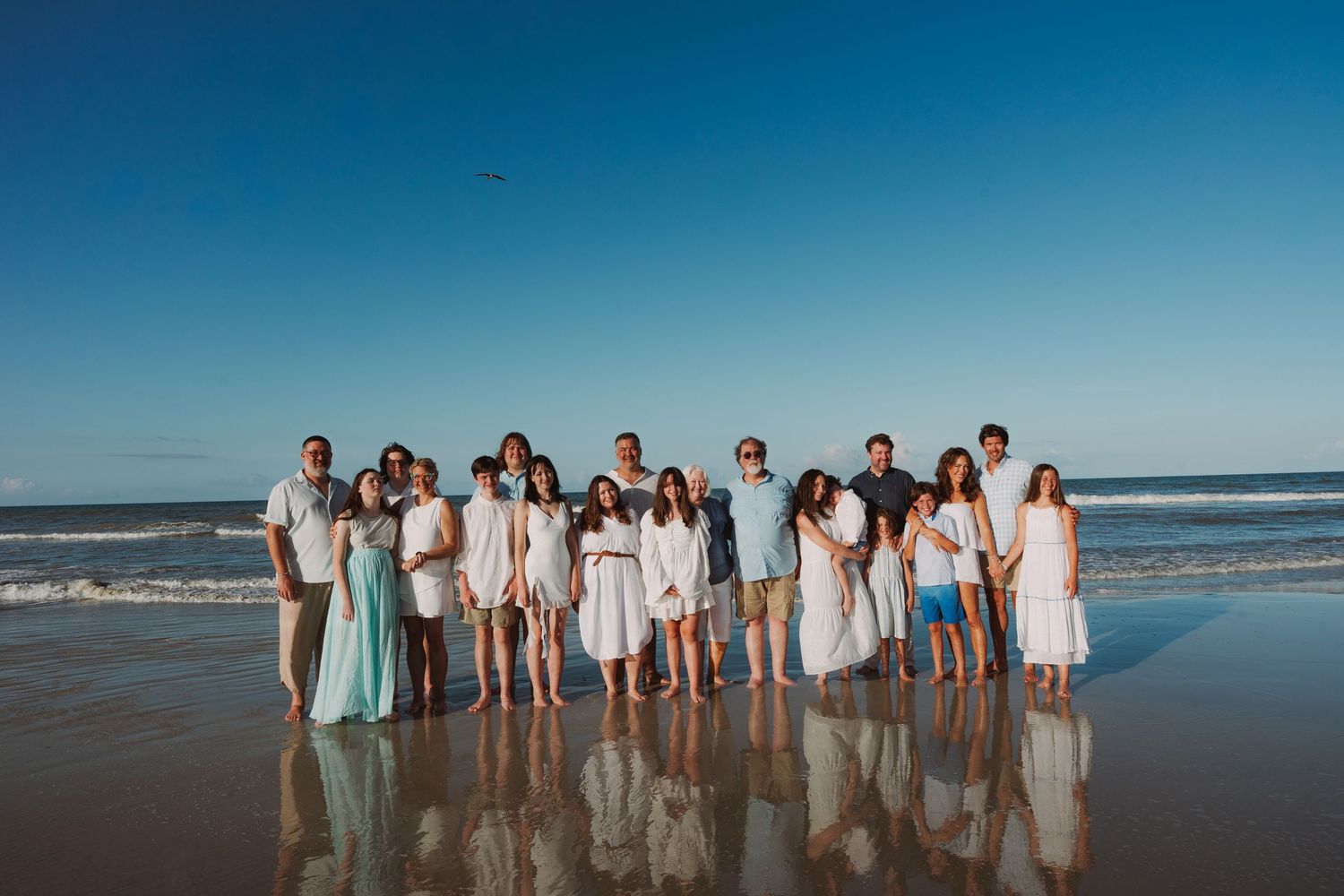 Large family group portrait on beach at golden hour wearing white and light blue outfits.