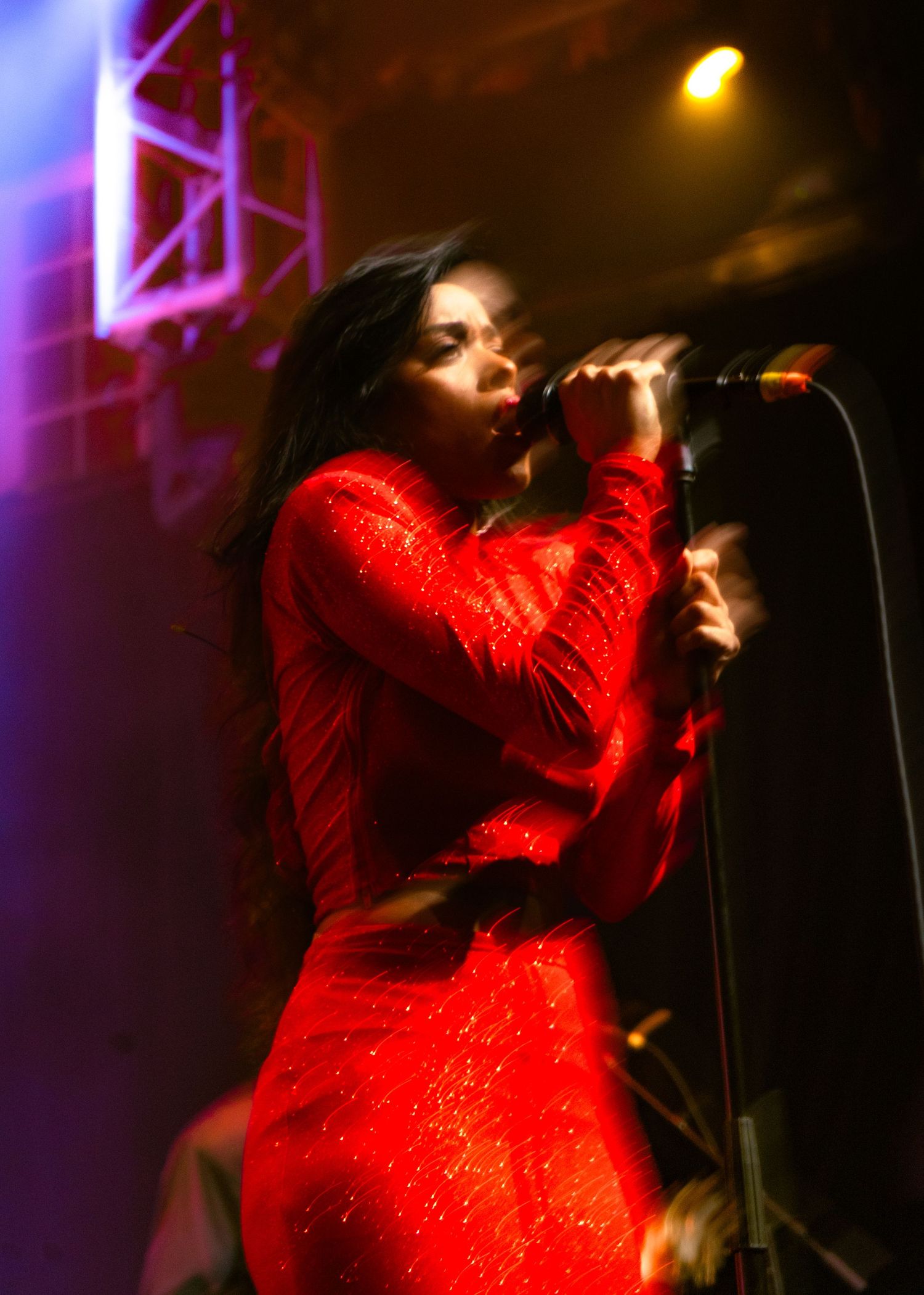 Female vocalist in a red sequin dress singing passionately into a microphone on stage.