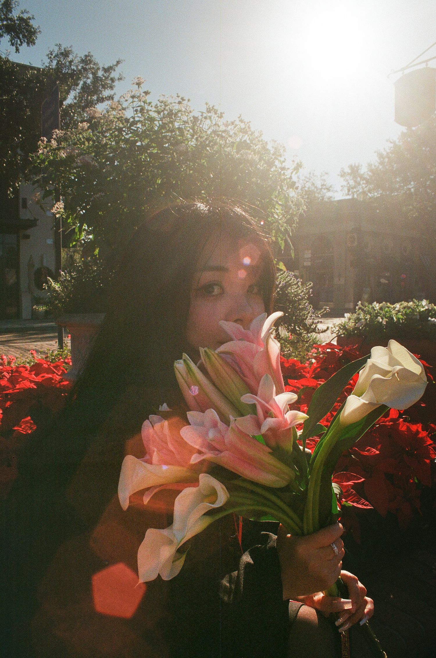 Woman holds bouquet of lilies and calla lilies in bright sunlit garden setting.