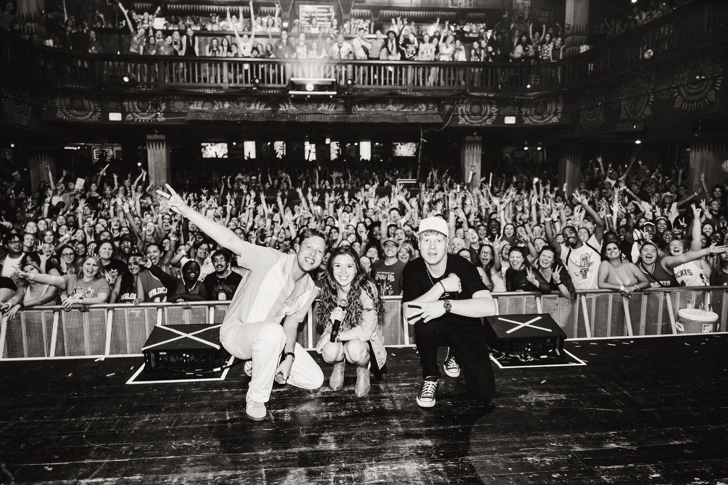 Black and white photo of performers and fans celebrating together in front of packed concert crowd.