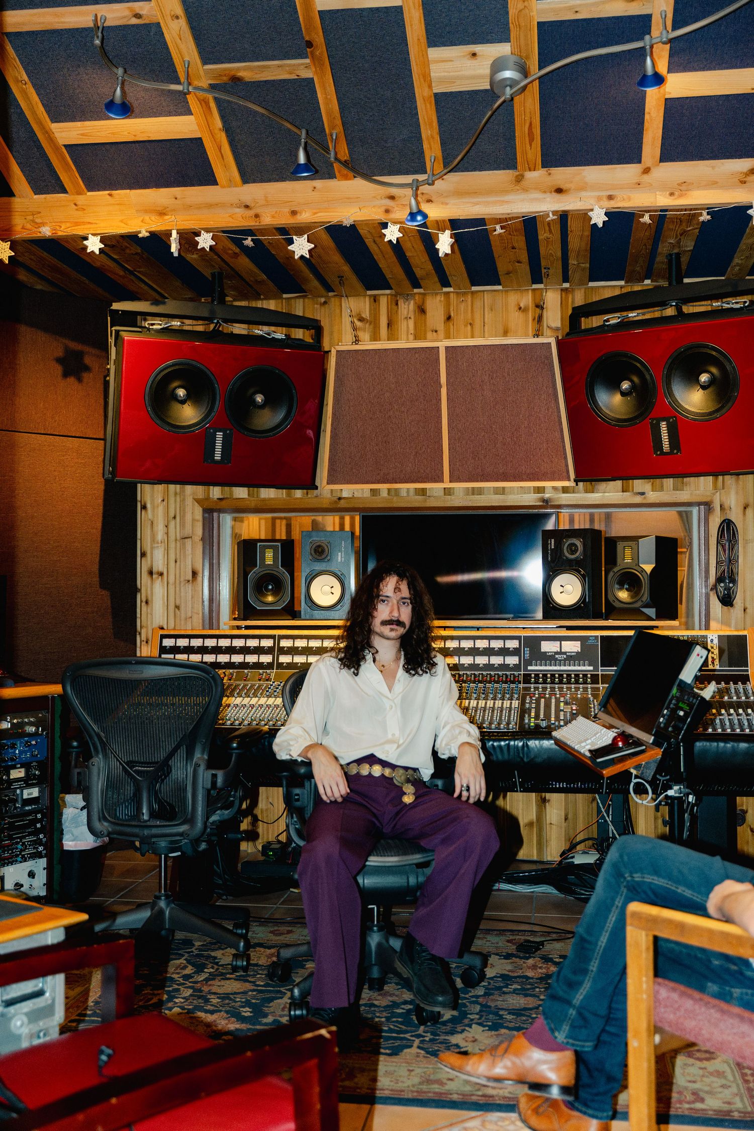 Long-haired musician with mustache sitting at large recording console in professional music studio.