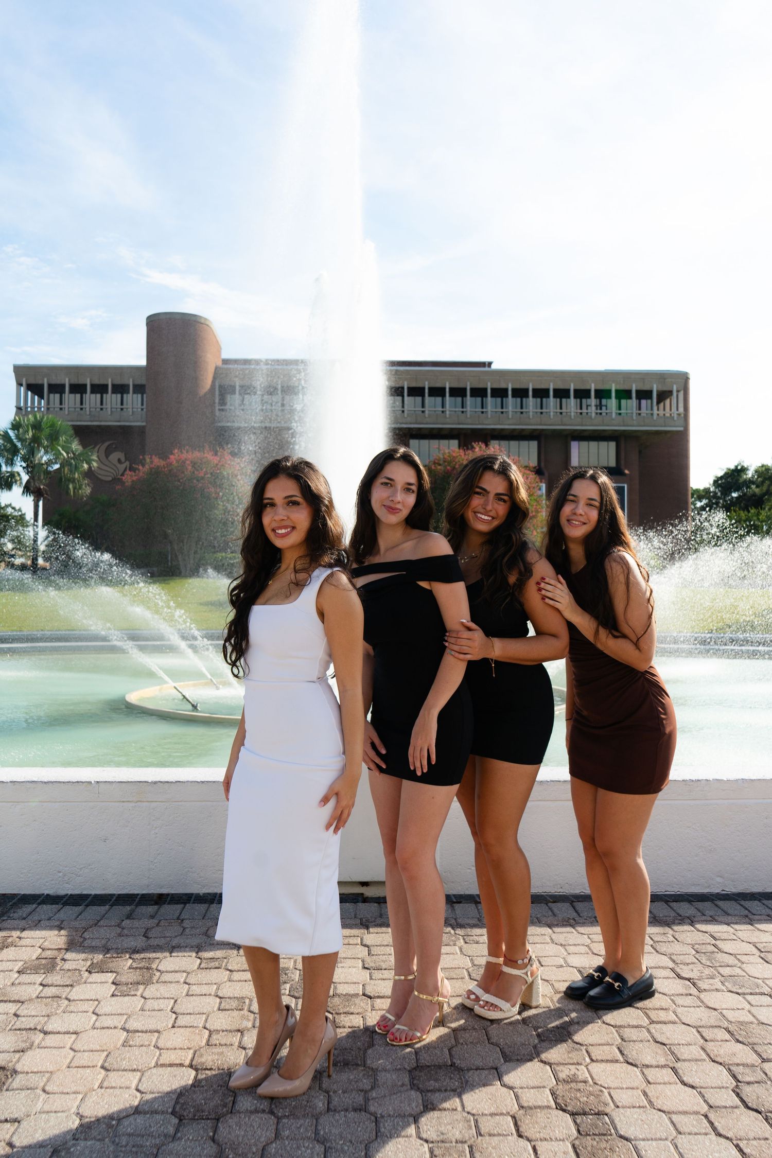 Four young women pose together near UCF campus fountain on a bright sunny day.
