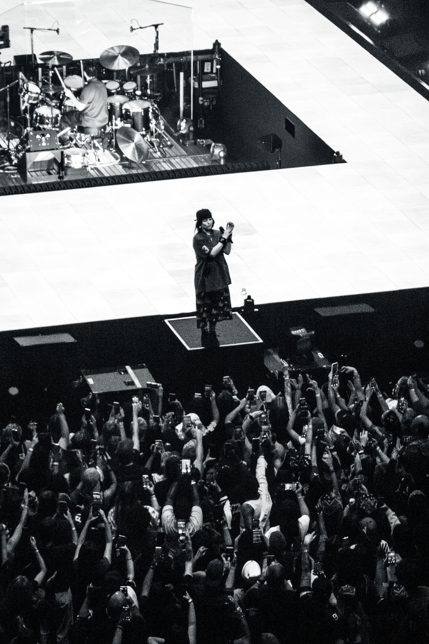 Black and white aerial view of a performer surrounded by a massive crowd holding up phones.
