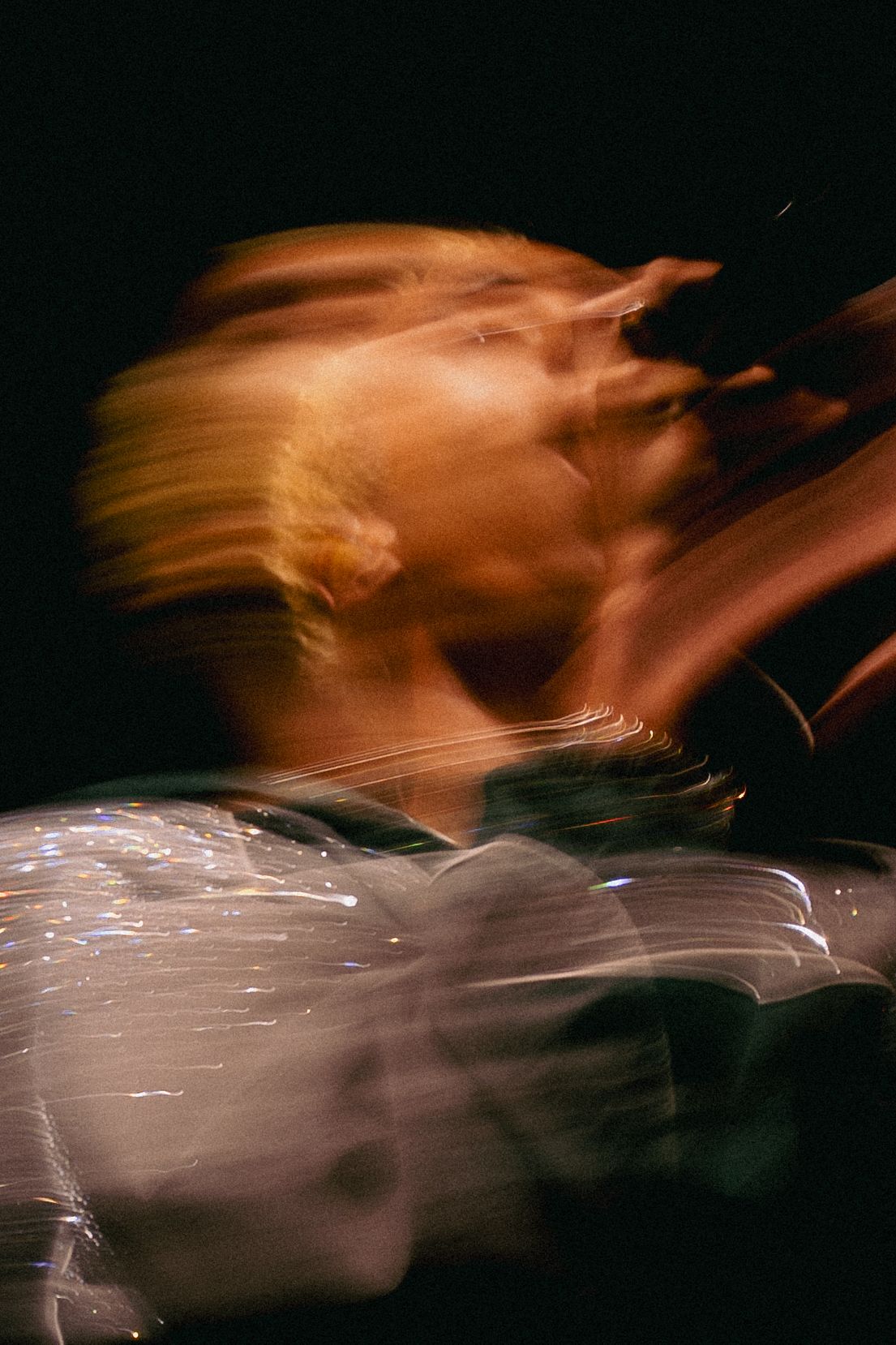 Abstract motion blur photography of a person with blonde hair against a dark background.