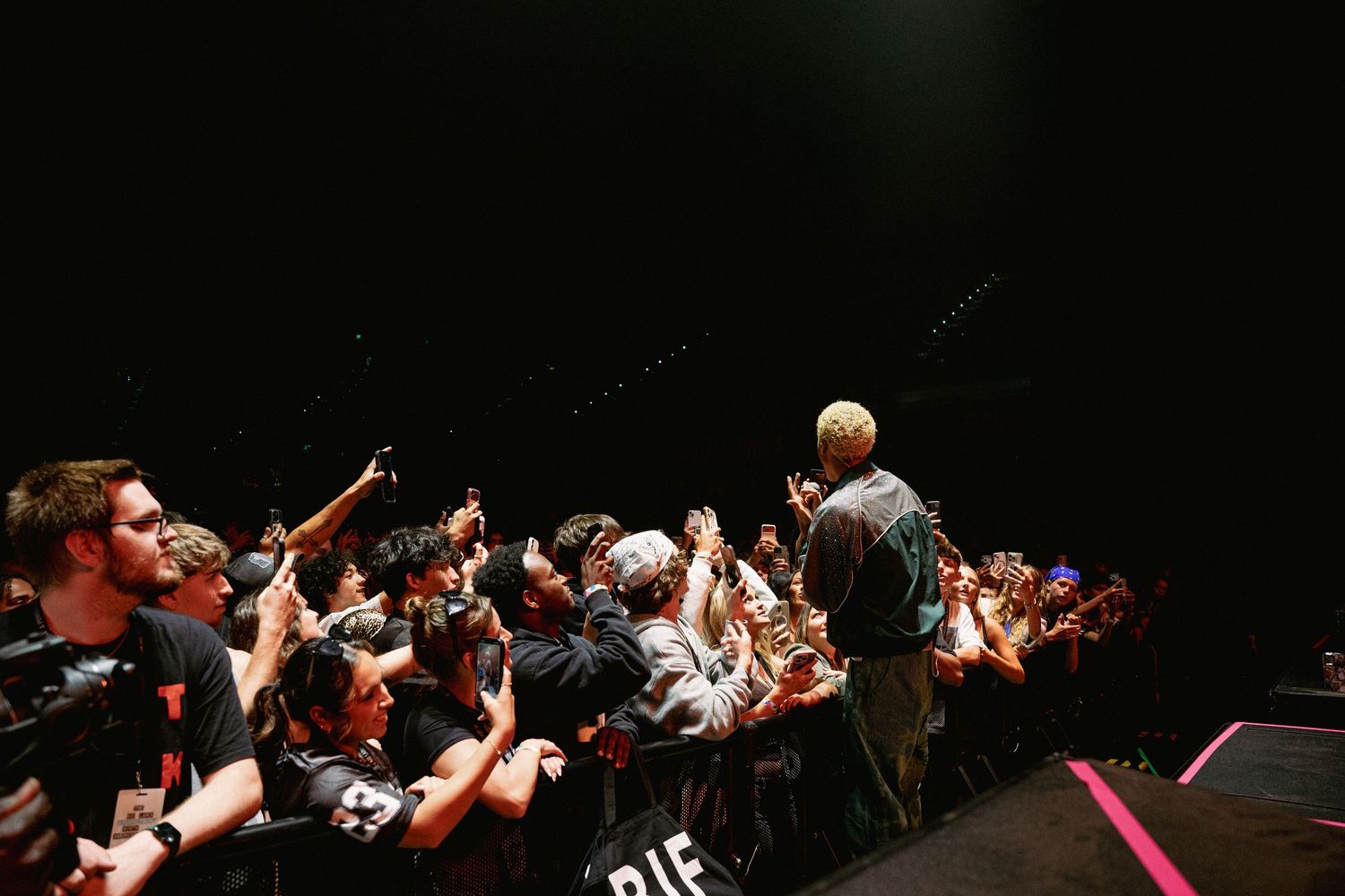 Performer on stage engaging with a large crowd at a live concert event in a dark venue.