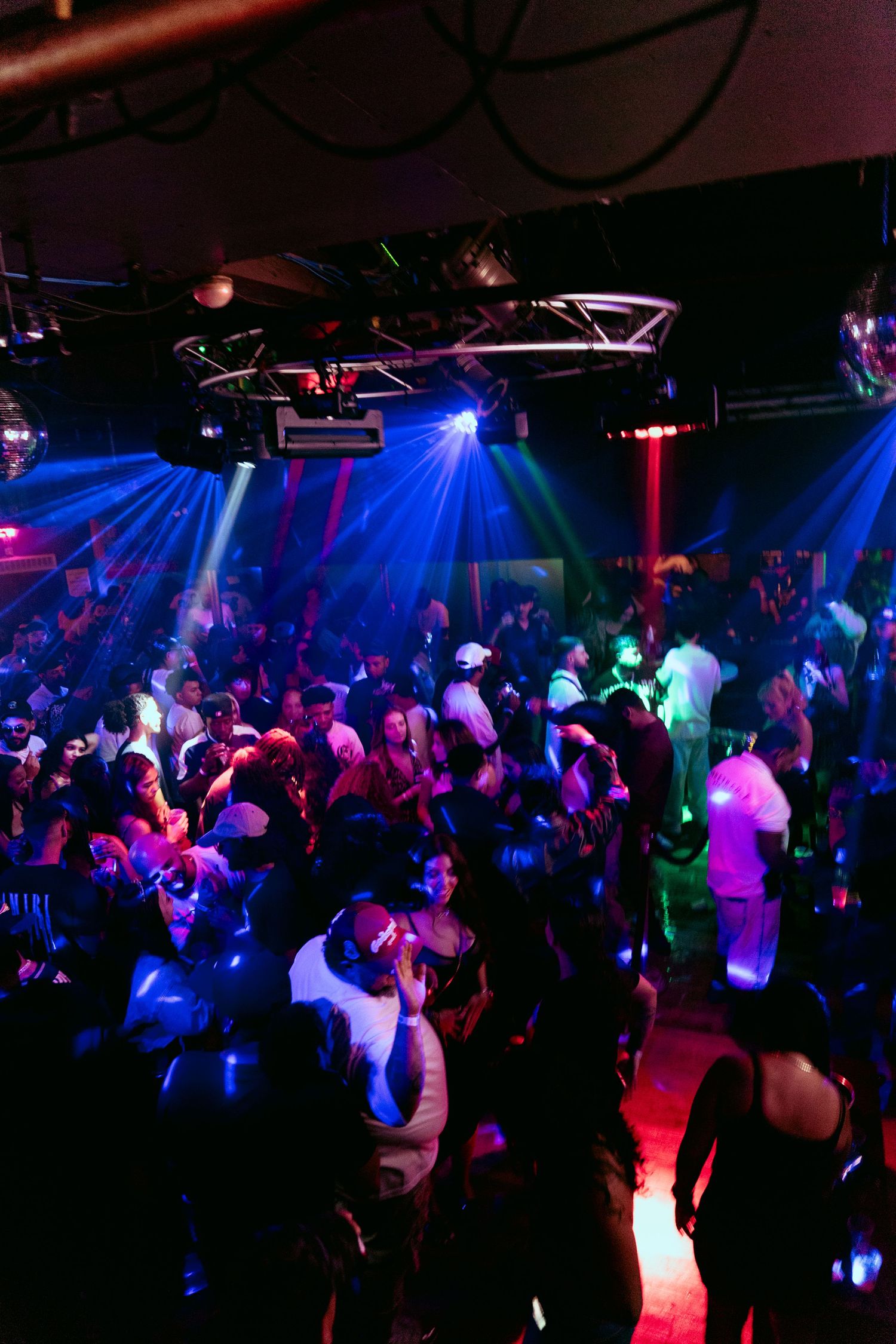 Crowded nightclub dance floor with colorful blue and red laser lights illuminating dancers in a dark venue.