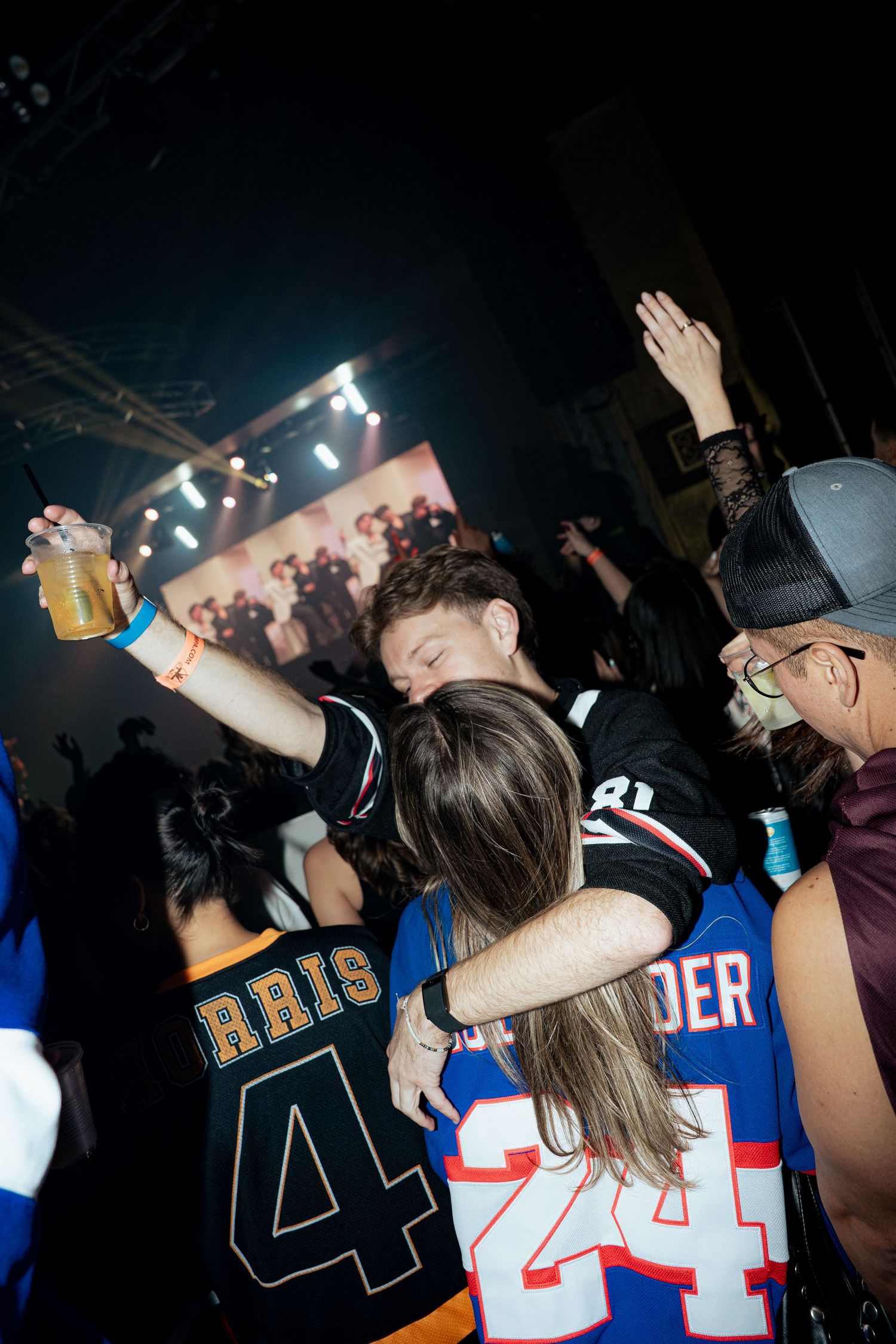 Two people hugging and dancing at a lively nightclub party, wearing sports jerseys.