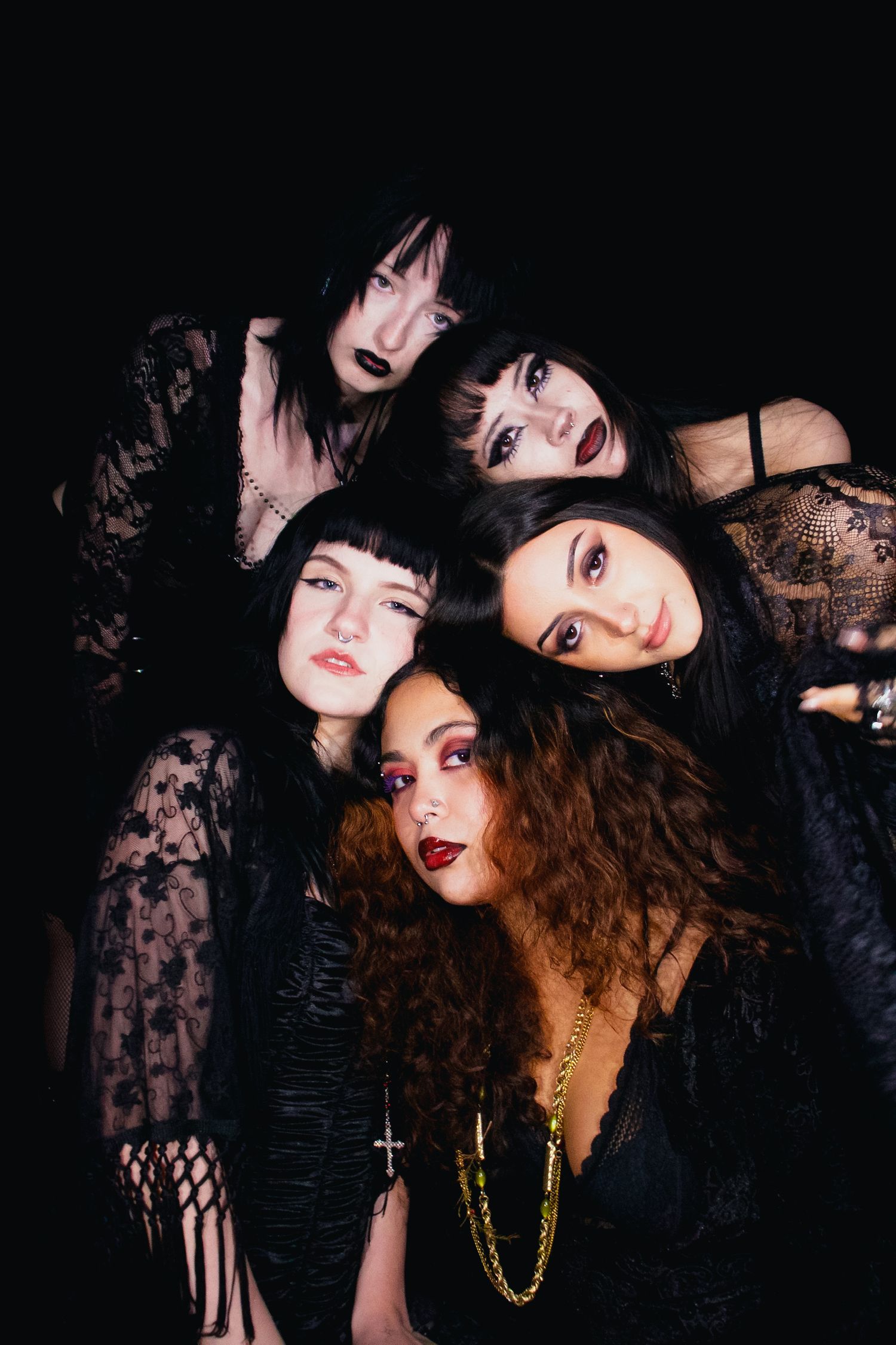 Group of five women in dark gothic fashion posing together against black background.