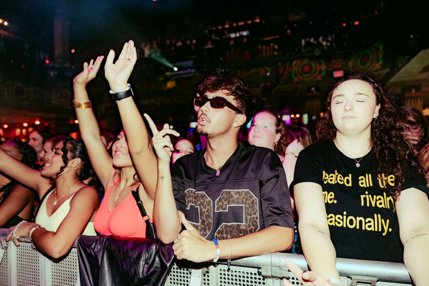 Excited concert fans crowd the barrier under colorful stage lights at a live music event.