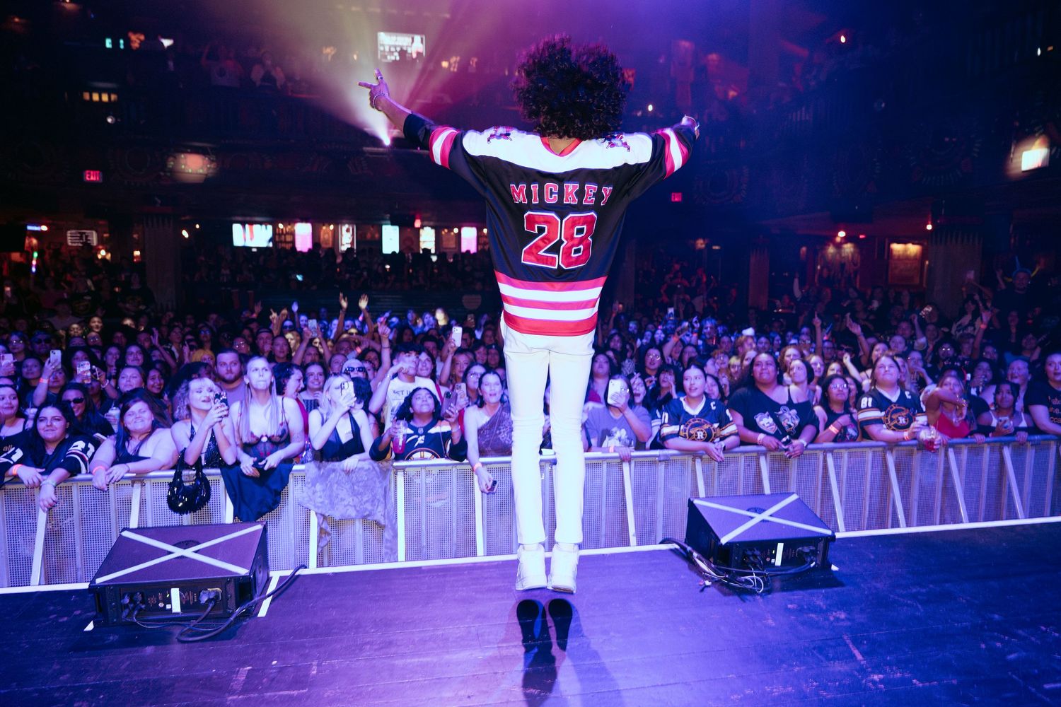 Performer in Mickey 28 jersey faces massive crowd at energetic indoor concert venue.