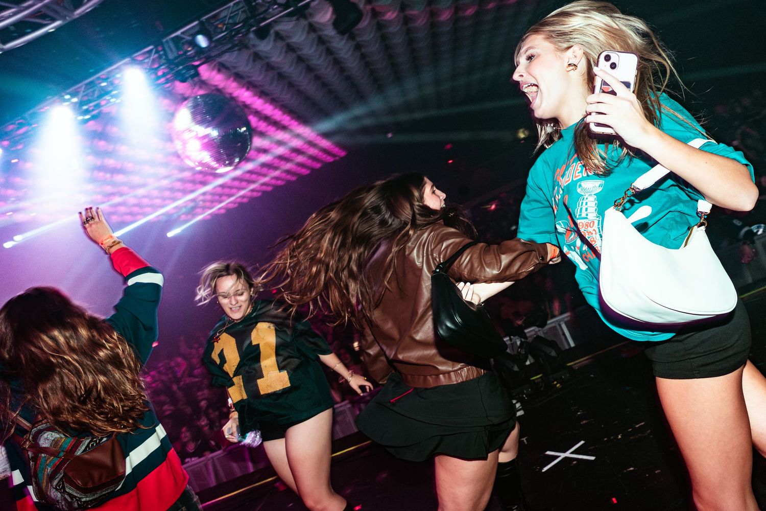 Young women dancing energetically at a nightclub party under colorful stage lights.