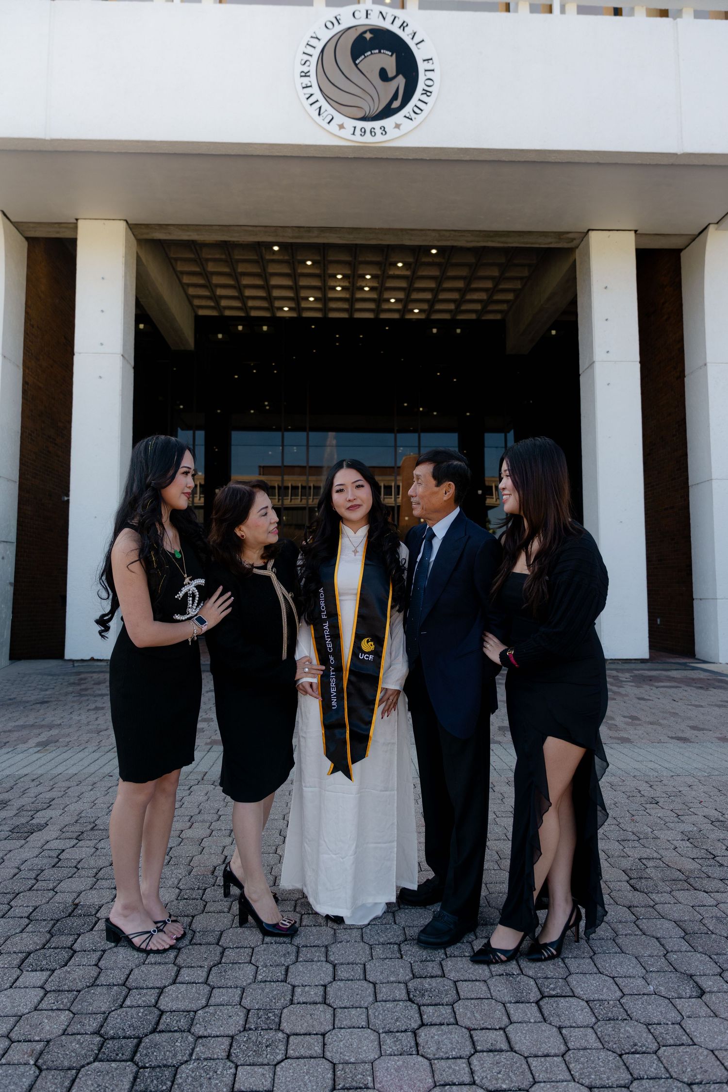 Graduate in white gown and UCF sash poses with family outside University of Central Florida.