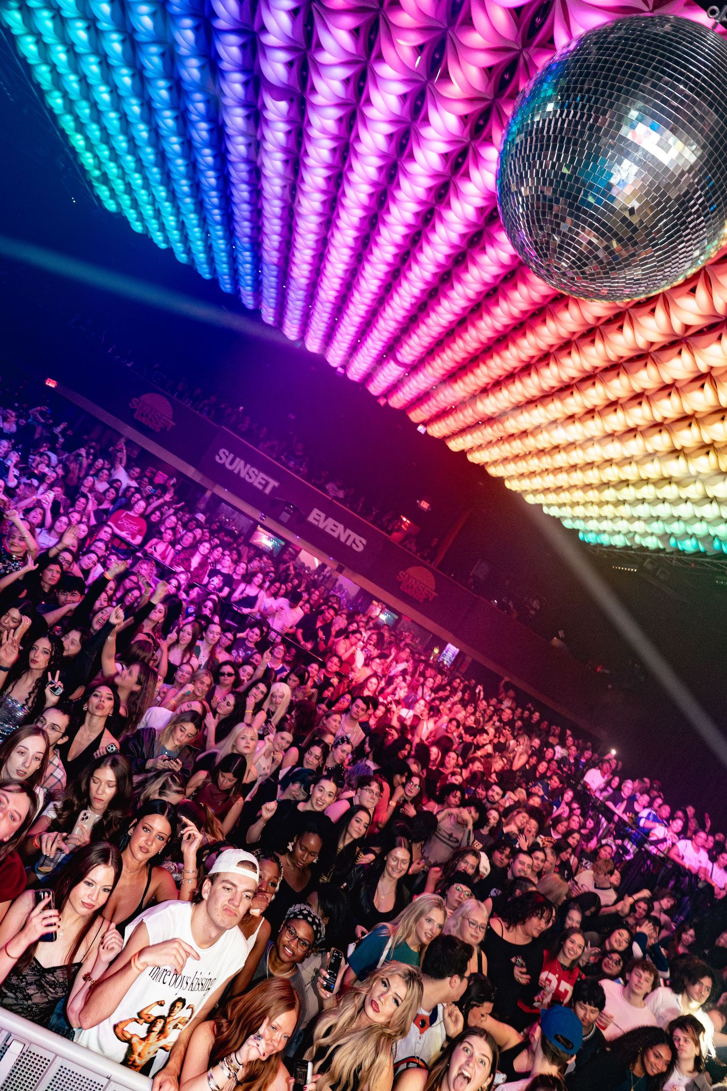 Packed nightclub crowd under rainbow LED lights and a disco ball at Sunset Events venue.