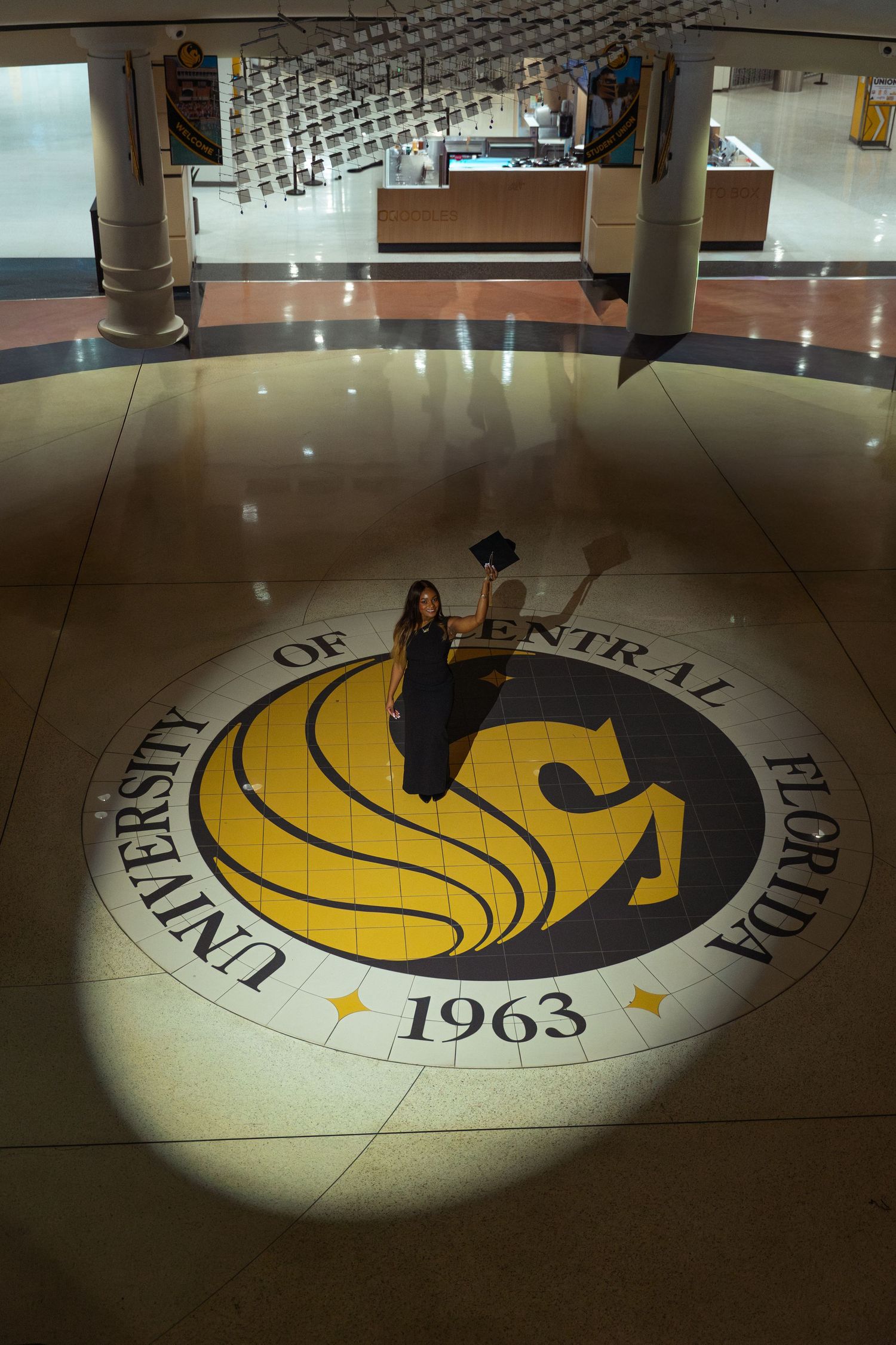 Graduate stands on University of Central Florida 1963 seal mosaic floor inside campus building.