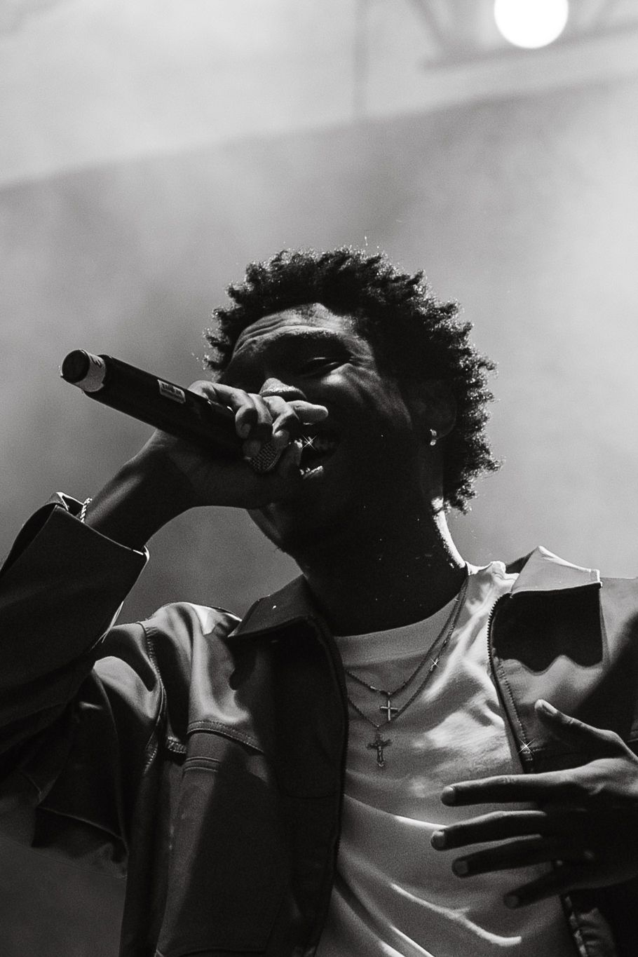 Black and white close-up of a male rapper performing with microphone and cross necklace.