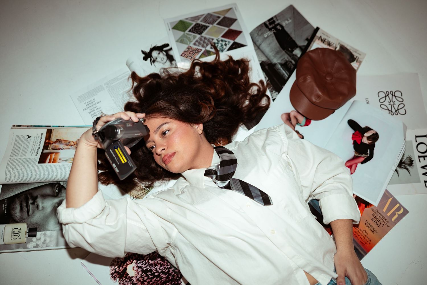 Two people lying on floor surrounded by magazines, woman holding camera with hair spread out.