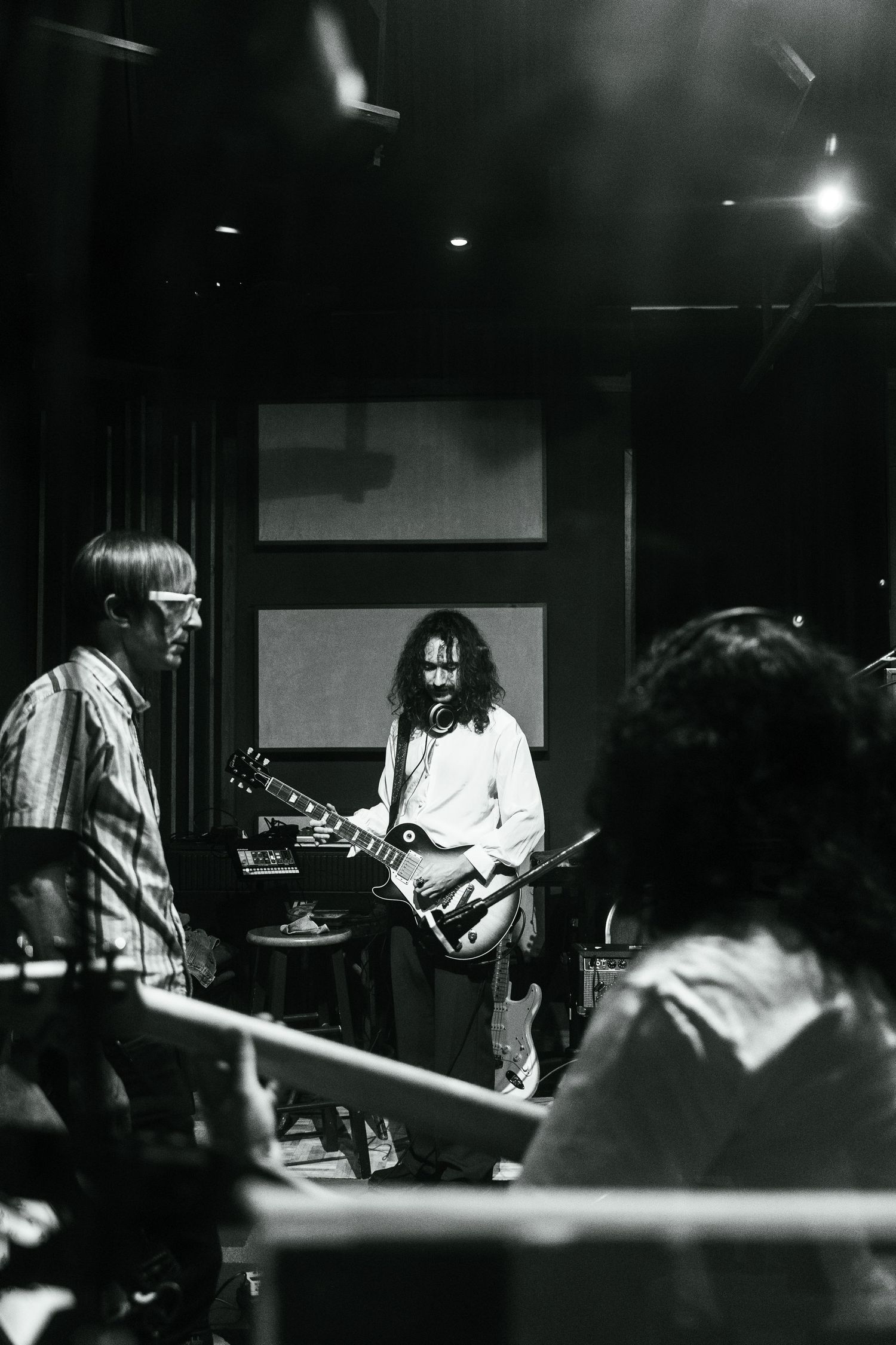 Black and white photo of guitarist with long hair playing electric guitar in dimly lit recording studio.