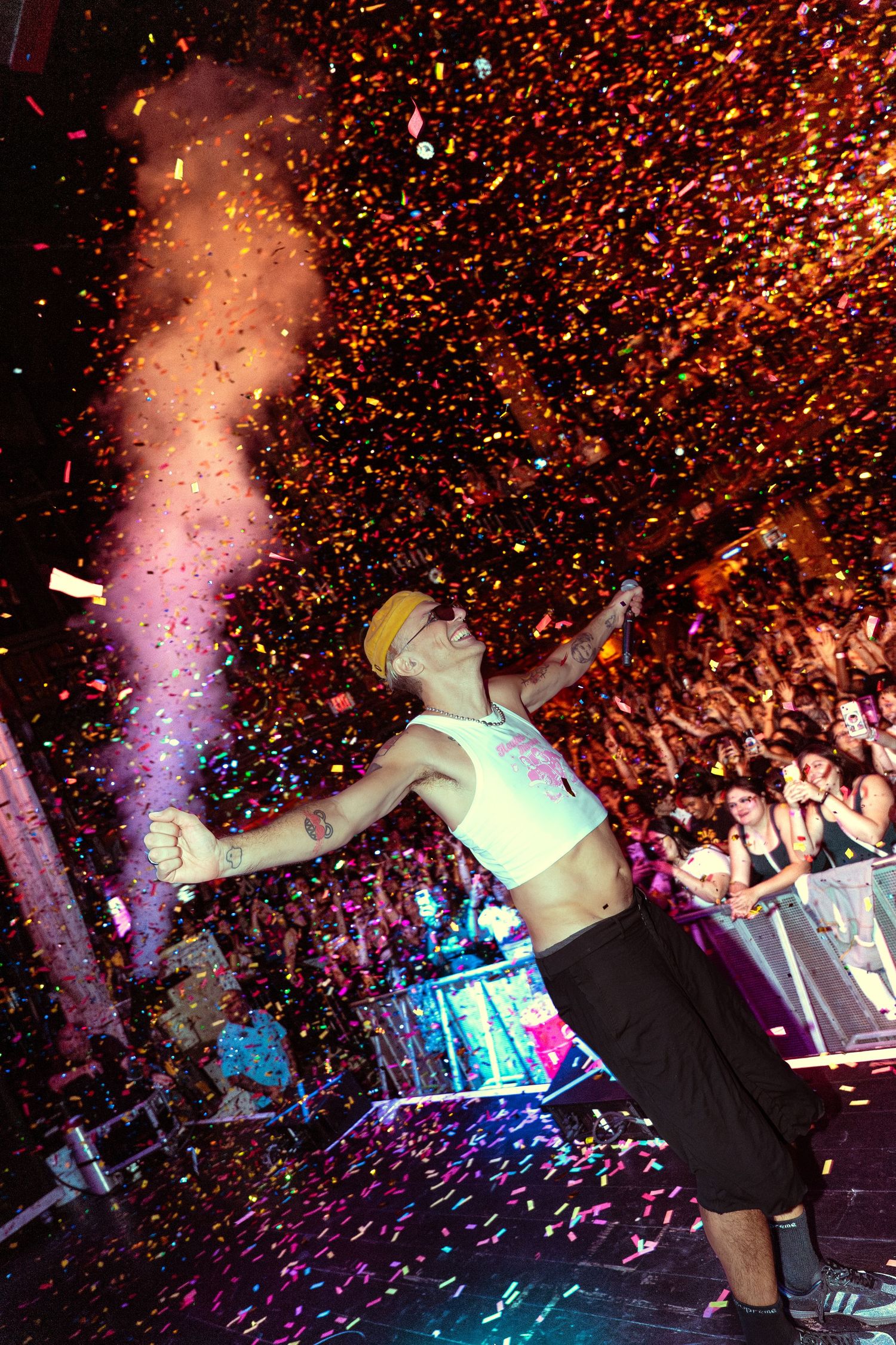 Performer celebrates on stage with colorful confetti explosion at a packed concert venue.