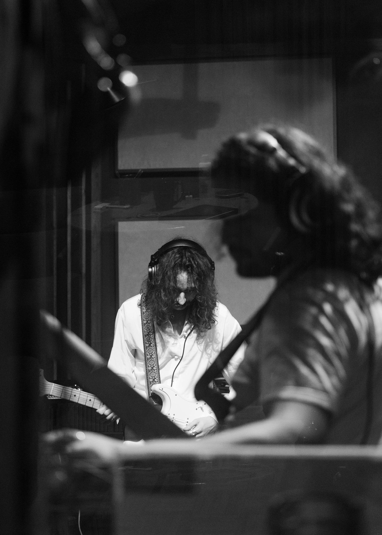 Black and white photo of a long-haired guitarist recording in a professional music studio.