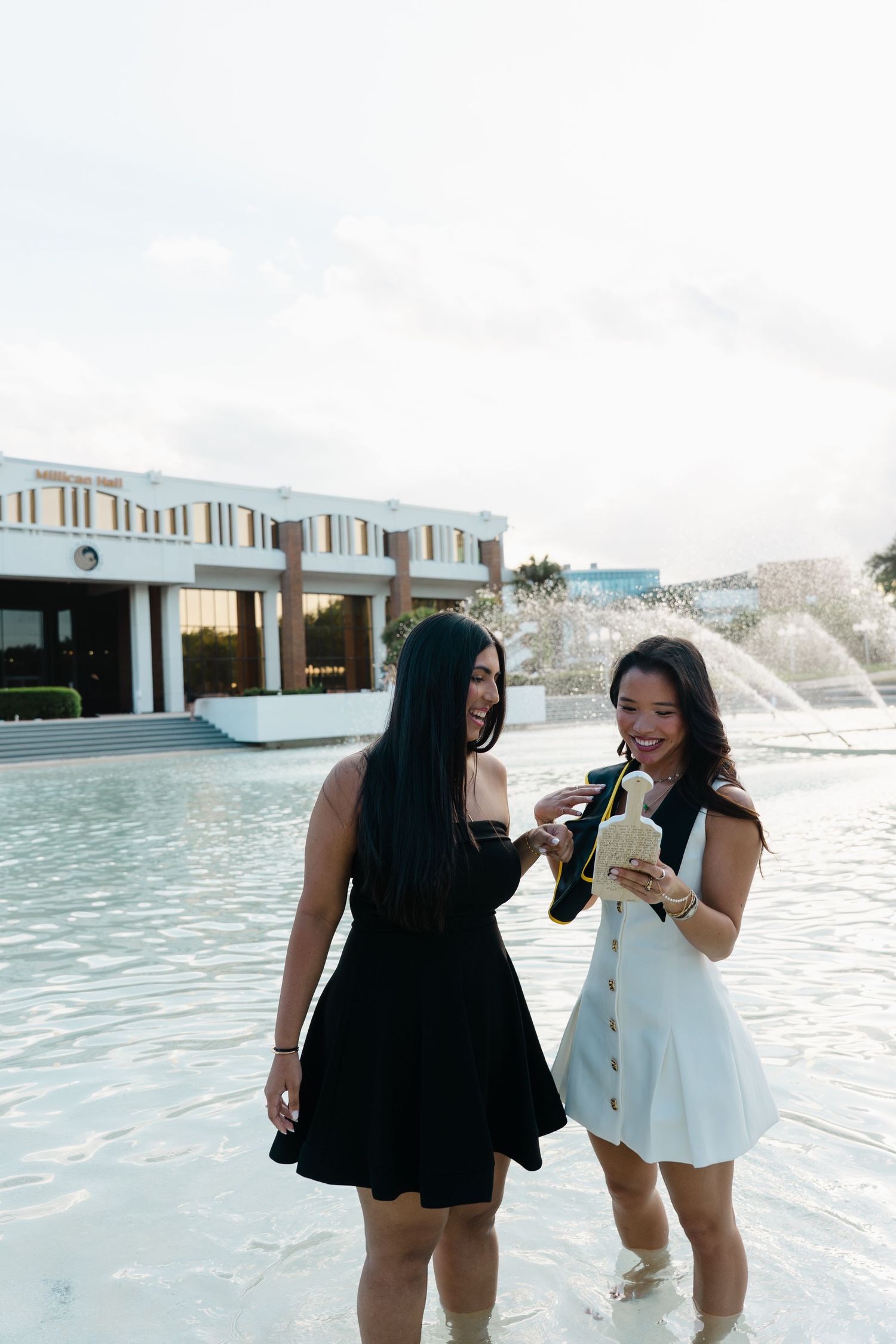 Two women in black and white dresses laughing near a fountain outside a resort.