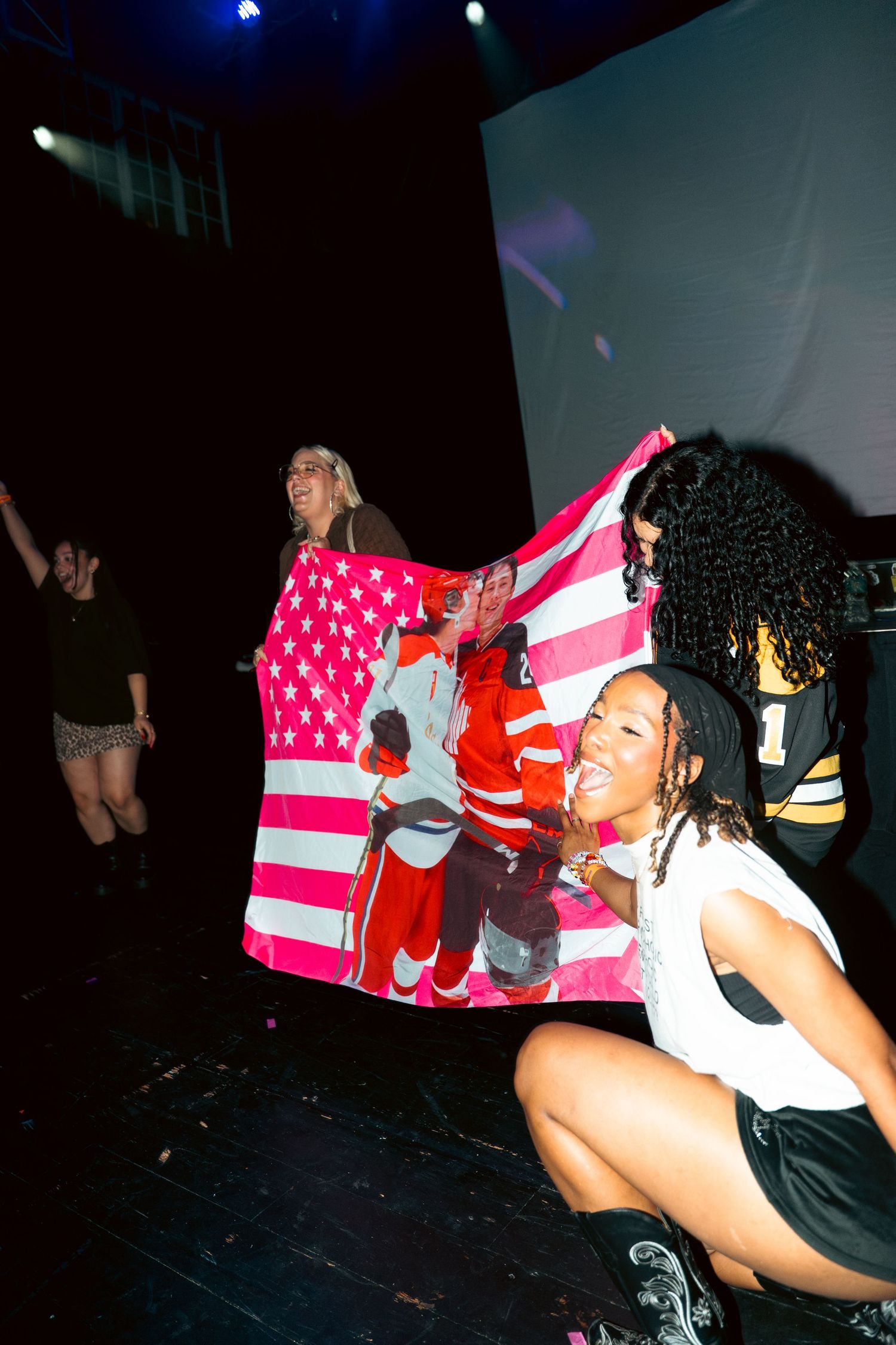 People celebrating with an American flag at an indoor event with projection screen in background.