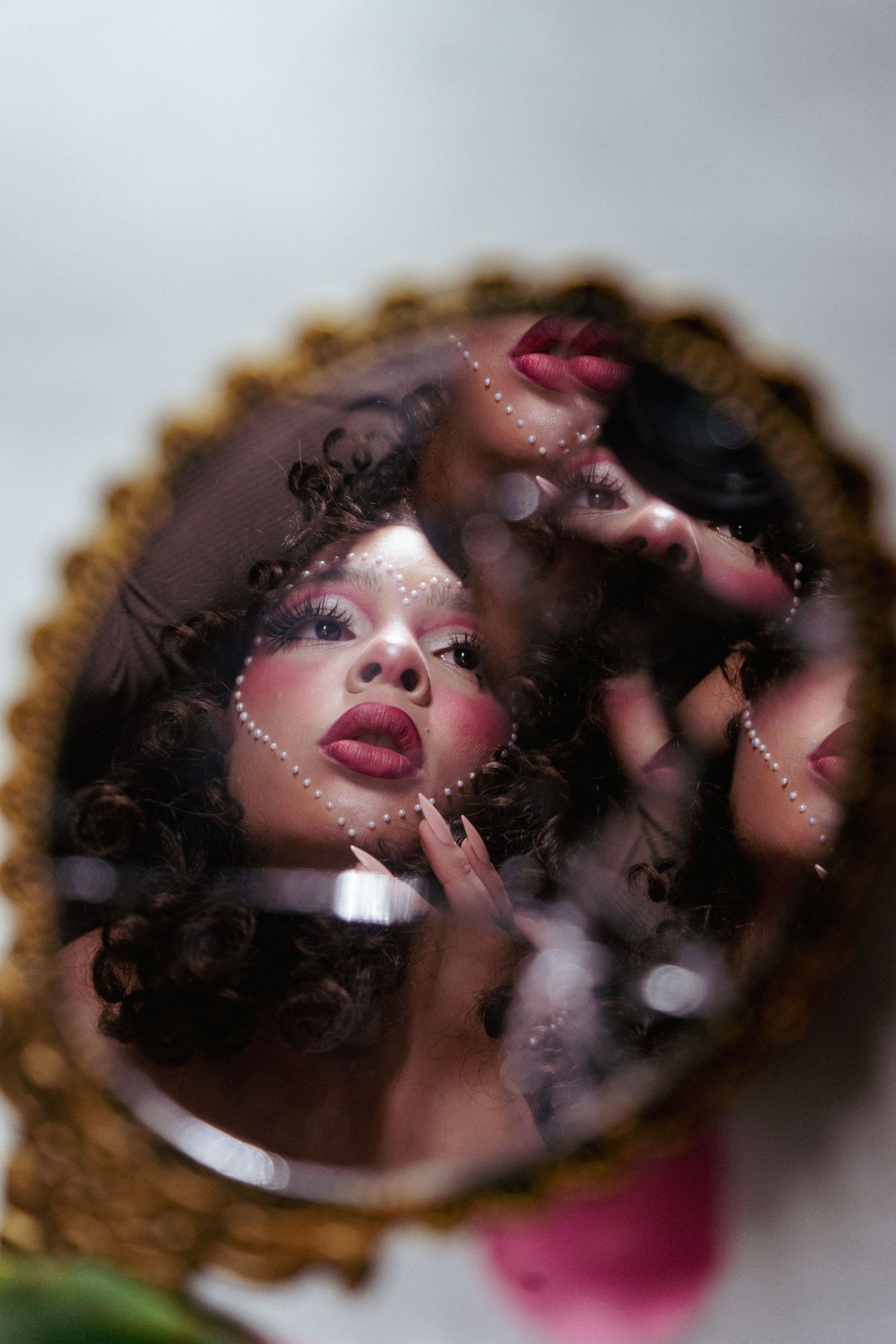 Woman with curly hair and dramatic makeup reflected in ornate vintage hand mirror.