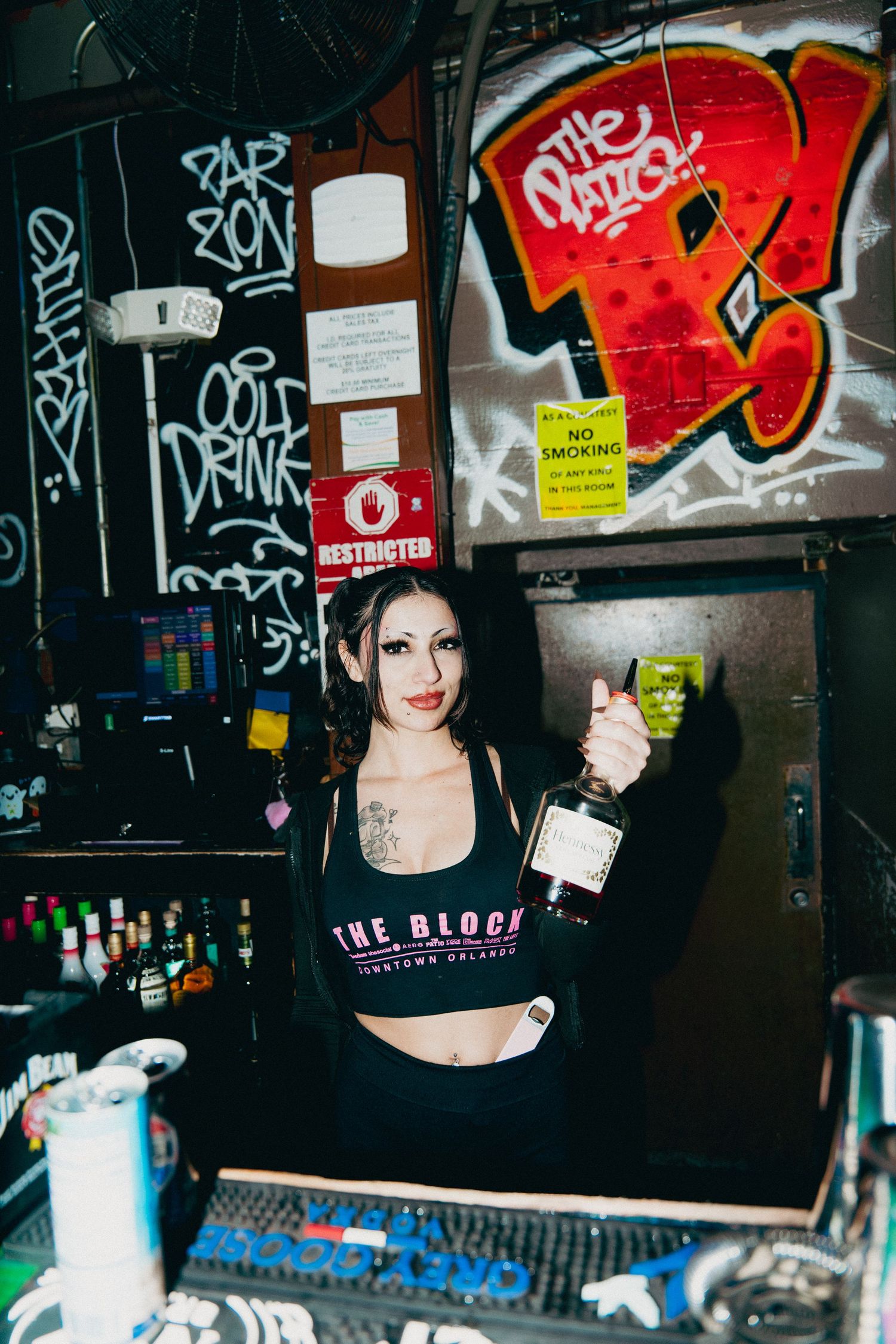 A tattooed bartender holds a liquor bottle at The Block bar in Downtown Orlando, surrounded by colorful graffiti walls.