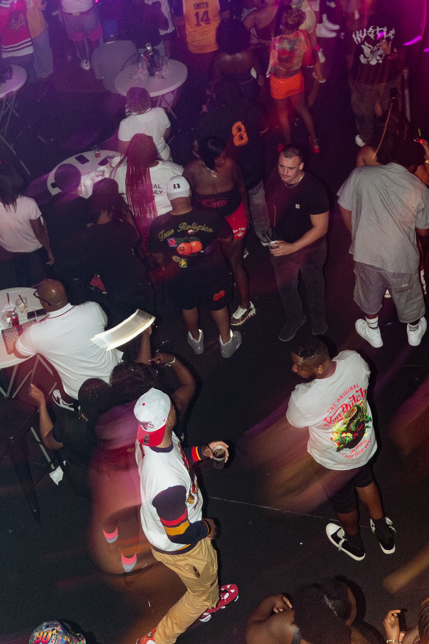 Crowd of people dancing and socializing at a nightclub party with purple lighting.