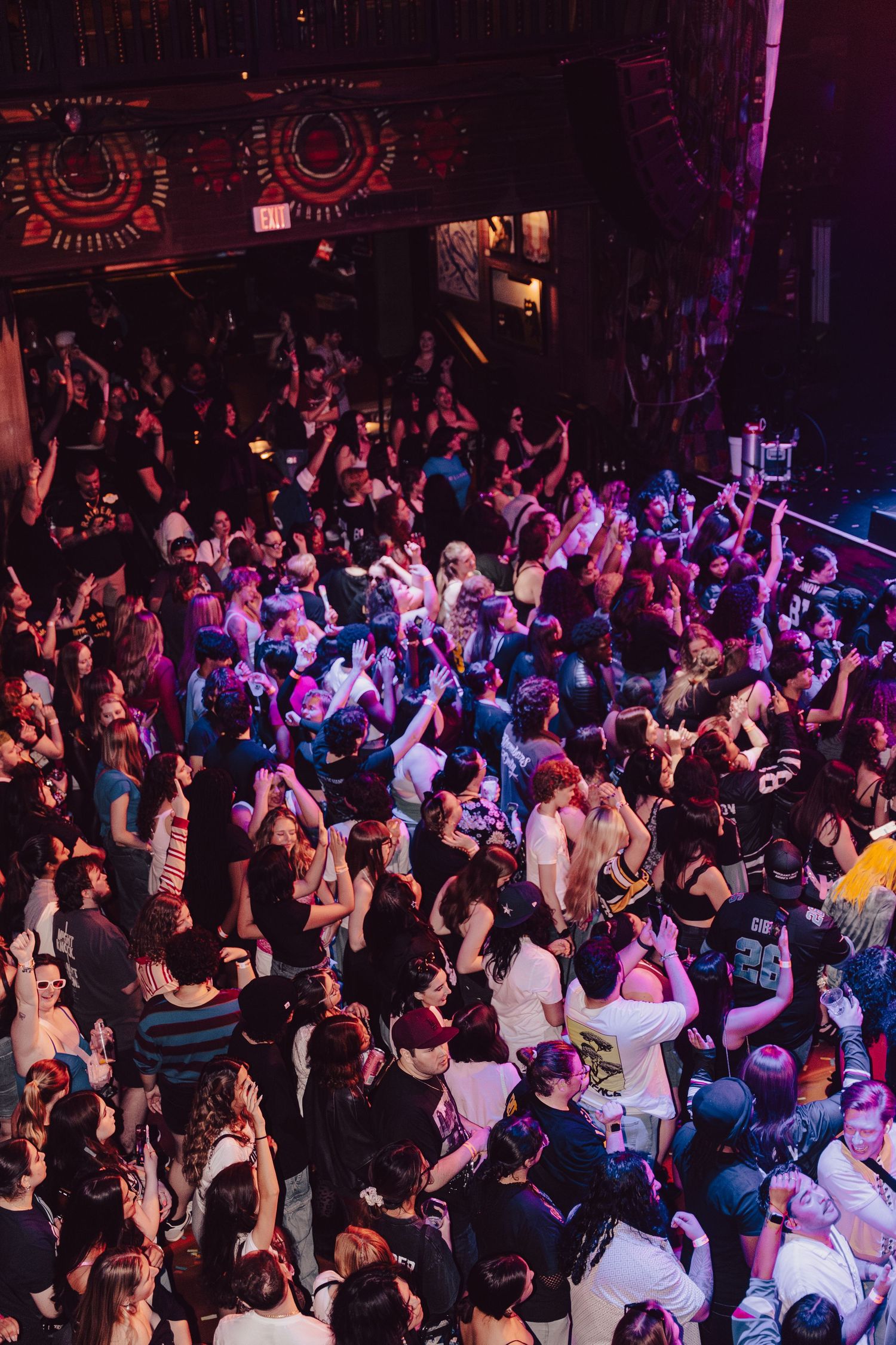Large crowd of people dancing and celebrating inside a packed nightclub with colorful lighting.