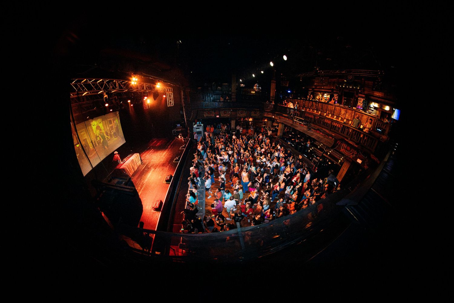 Wide fisheye aerial view of a packed concert venue with warm orange stage lighting.