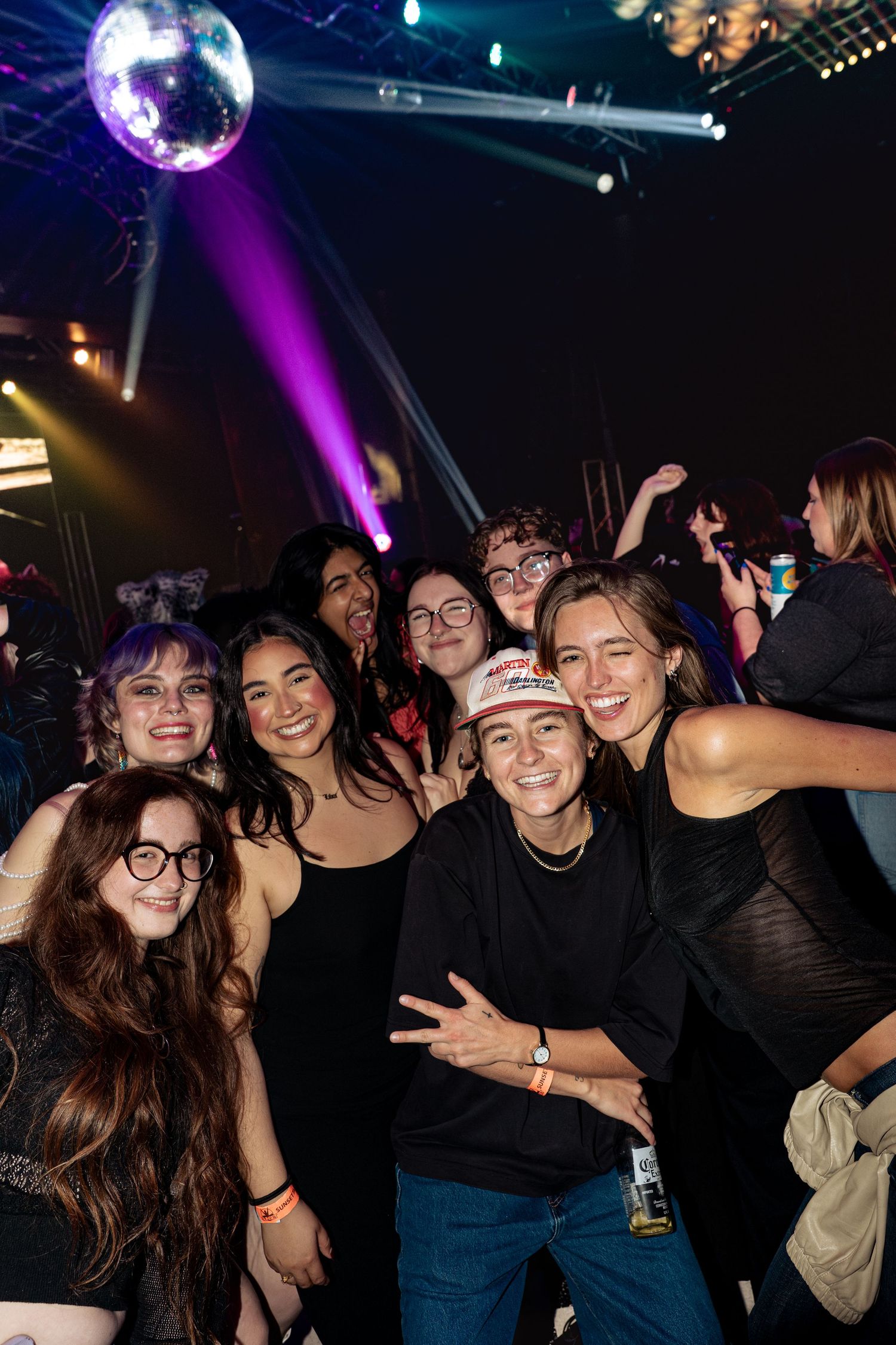 Group of friends smiling together at a nightclub with disco ball and purple stage lights.