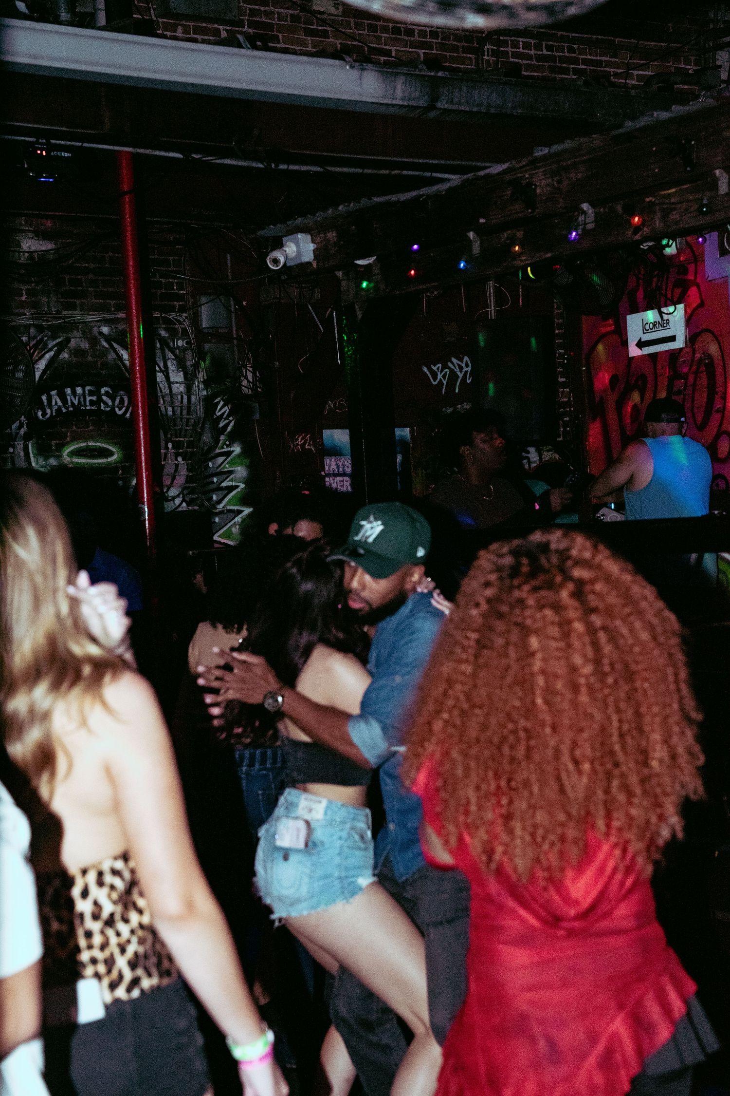 People dancing and socializing at a lively nightclub with colorful lights and brick walls.