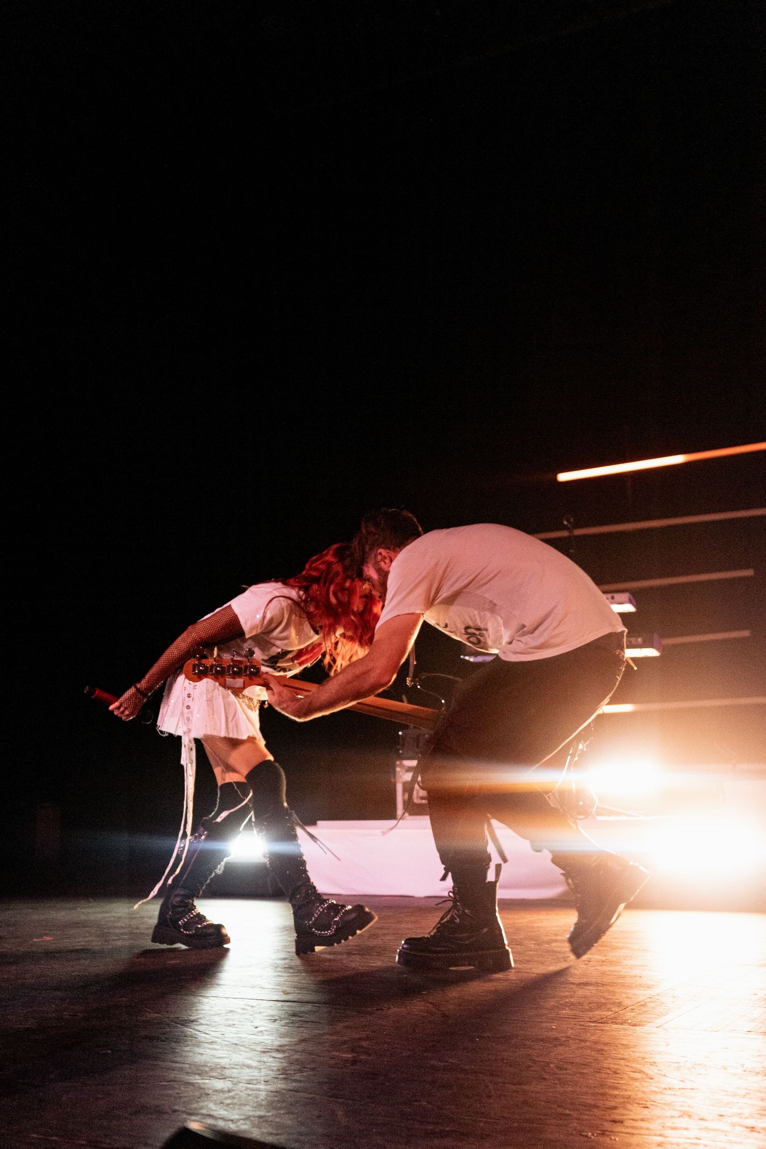 Two performers crouching on stage under dramatic golden spotlight during live concert.