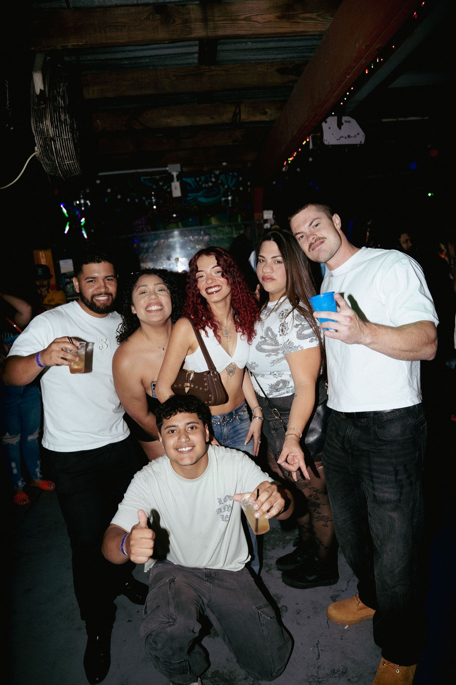 Group of six friends smile and pose together at a lively nightclub party.