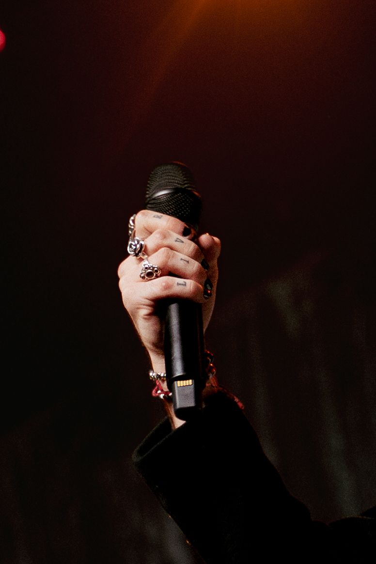 Close-up of a hand holding a microphone with multiple rings under warm stage lighting.
