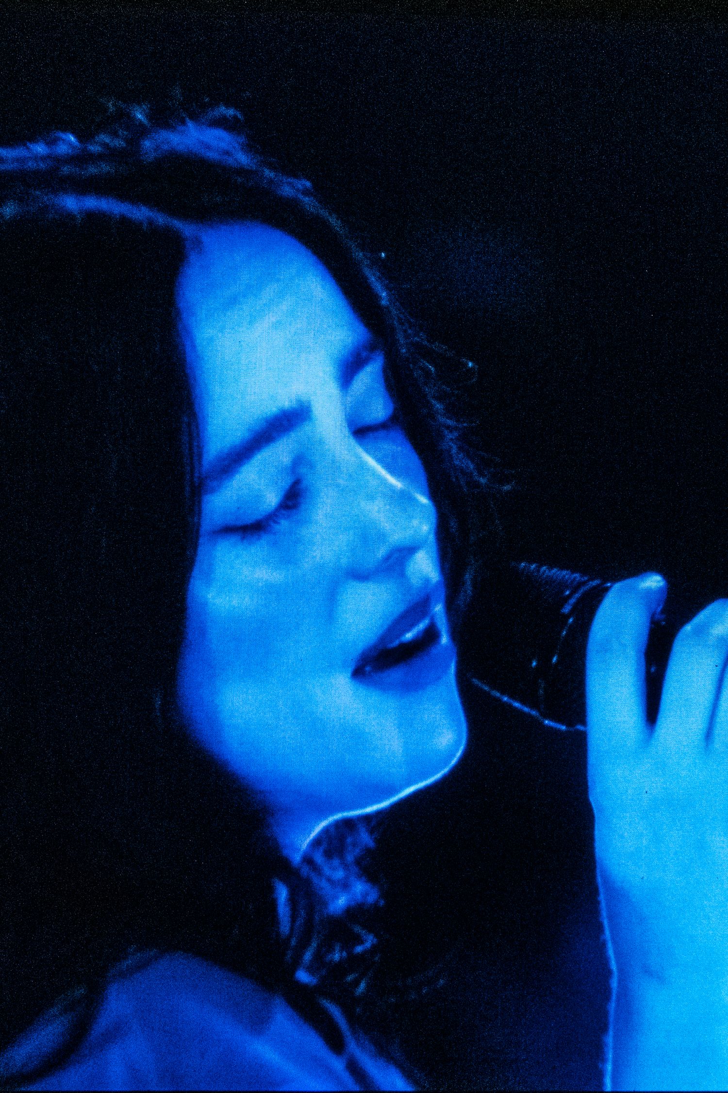 Female singer performing passionately on stage bathed in blue lighting holding a microphone.