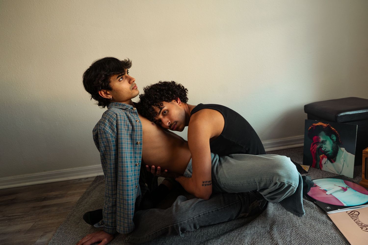 Two young people share an intimate moment sitting on the floor in a cozy room.
