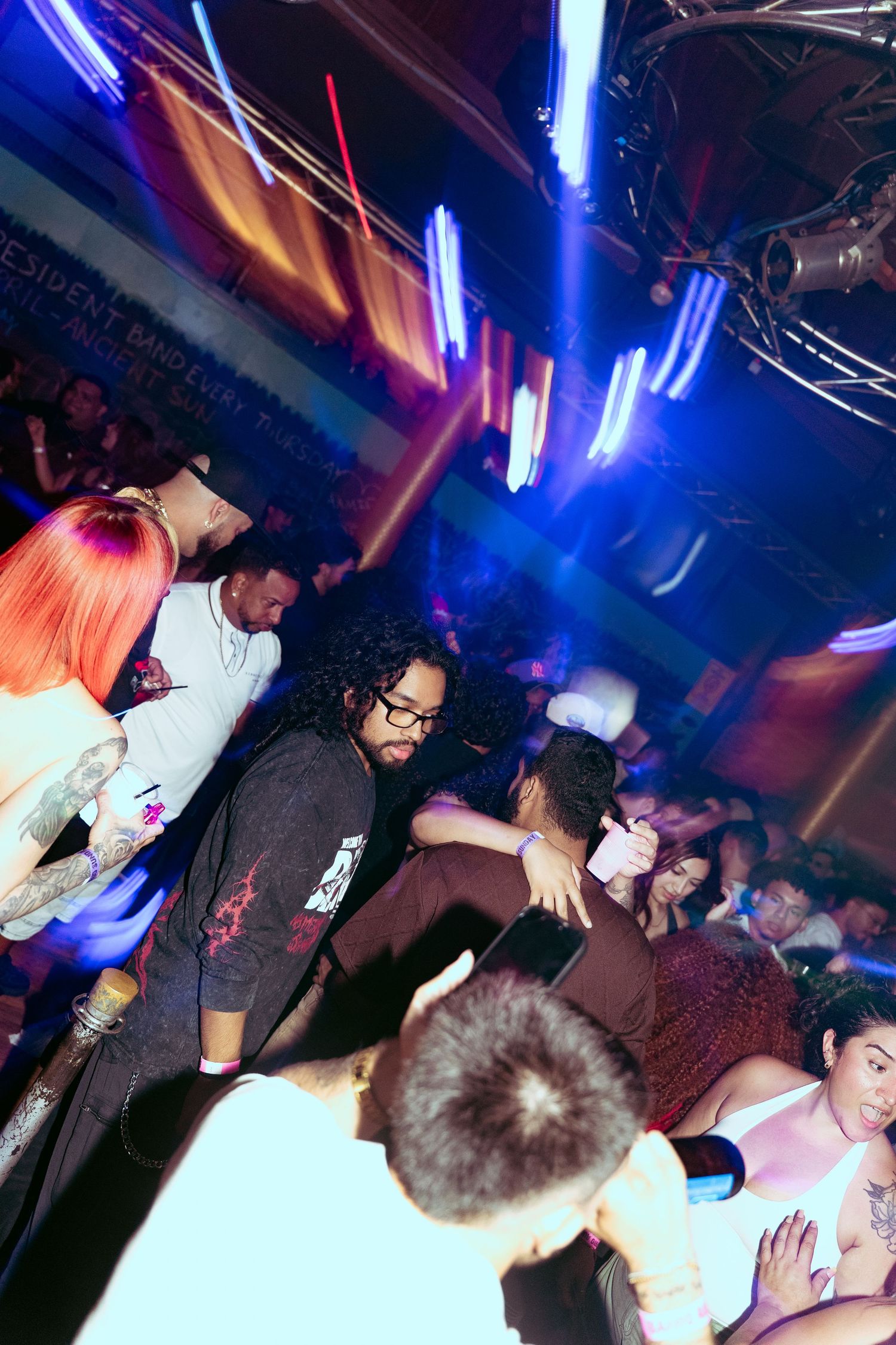 Crowded nightclub scene with colorful neon lights, diverse partygoers dancing and socializing on a packed dance floor.