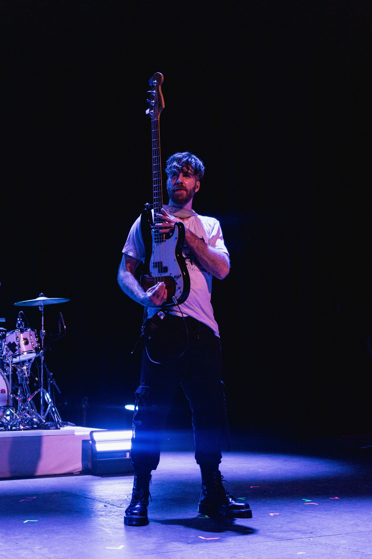 Male guitarist holding black electric guitar on stage under blue concert lighting.