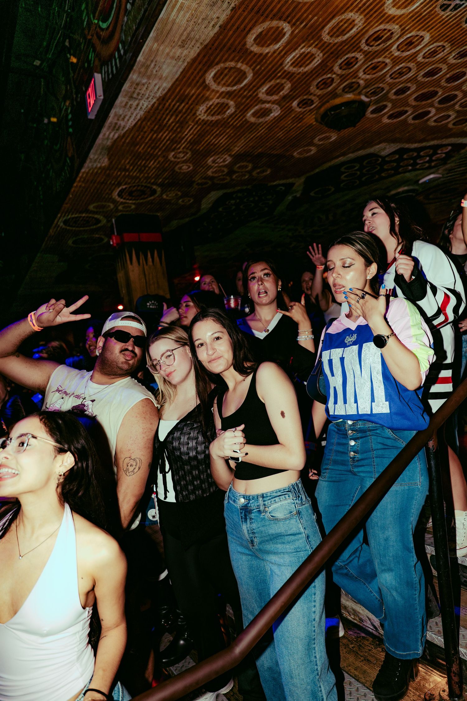 Crowd of young people dancing and posing at a nightclub party, with colorful lights and decorative ceiling.