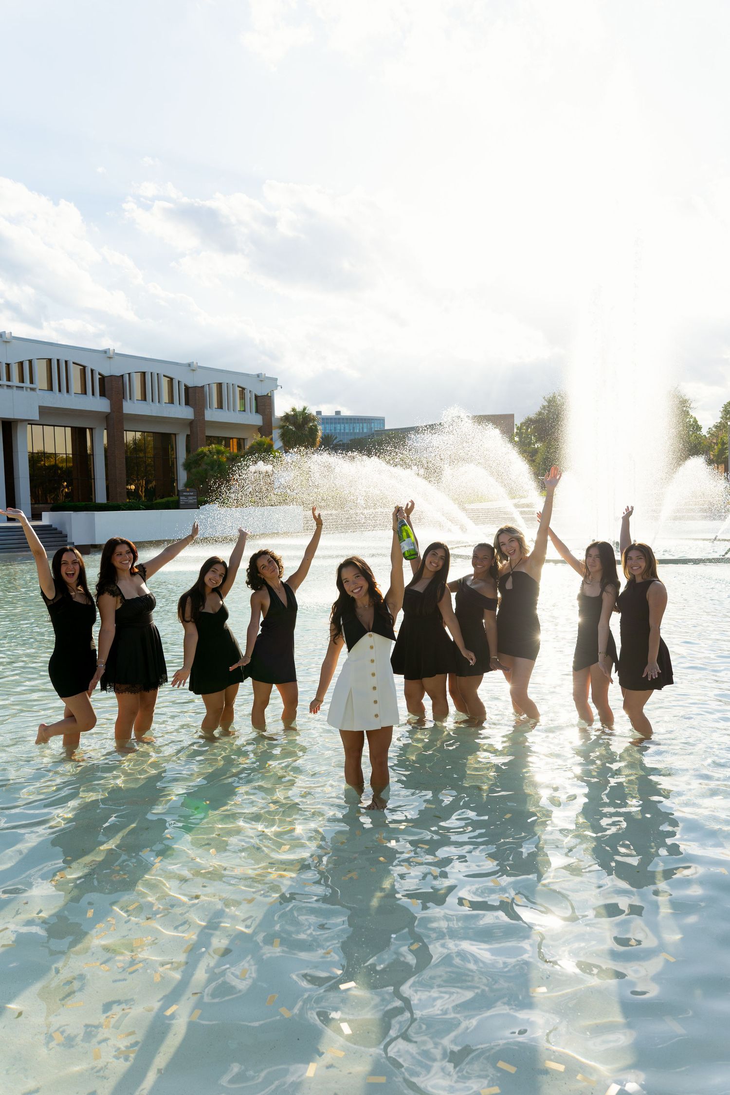 Group of women in black dresses celebrating in a fountain, with one woman in white leading the fun.