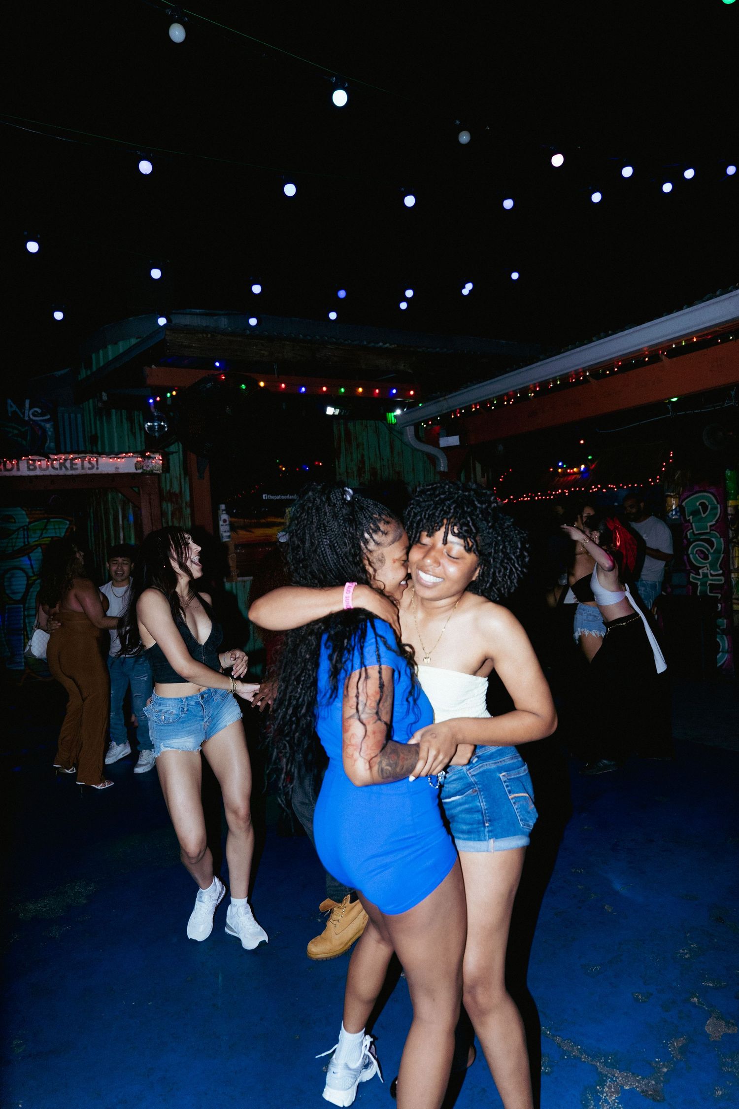 Two women dancing and embracing joyfully at a vibrant nightclub with colorful lights.
