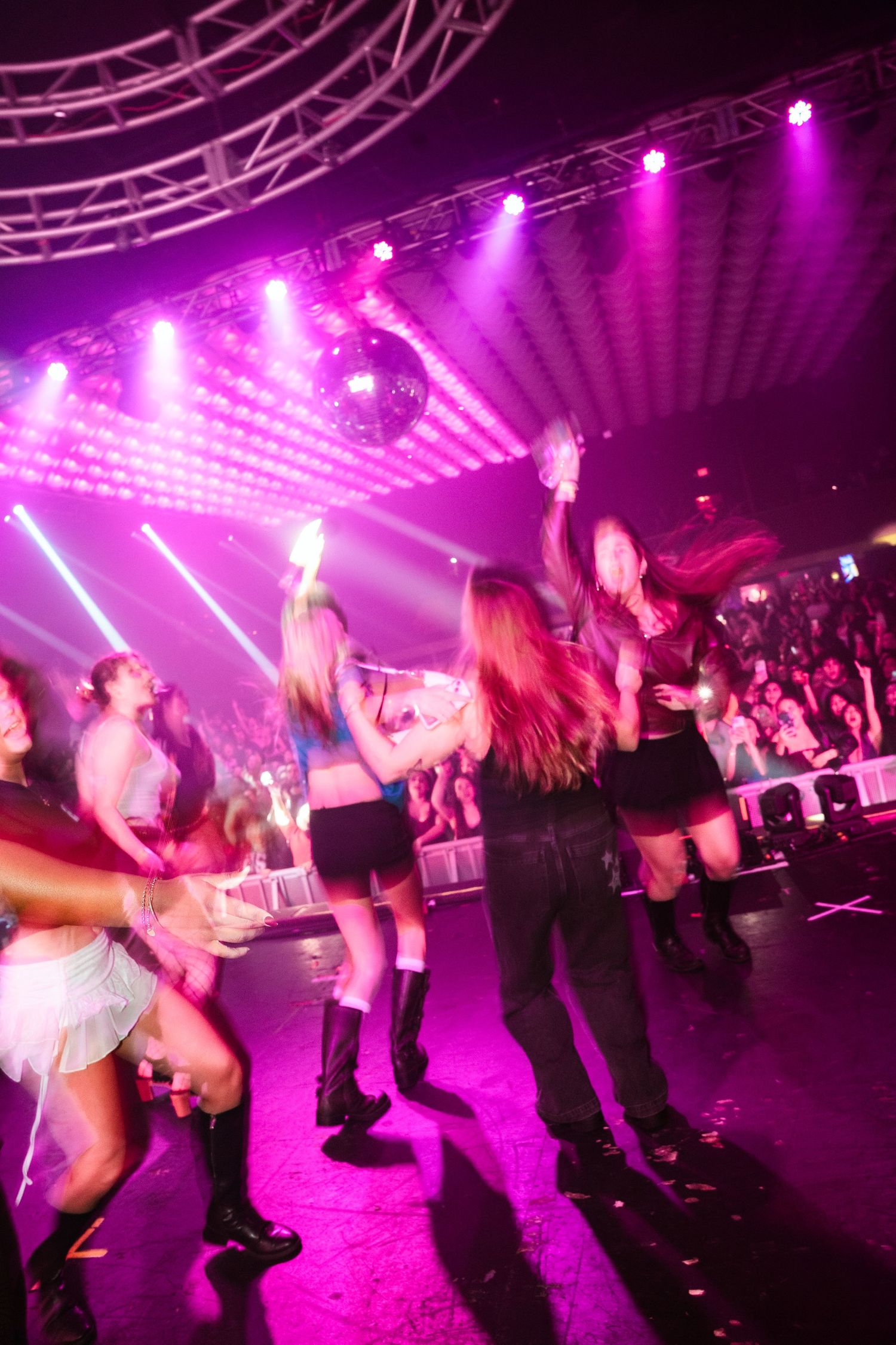 Female dancers performing on a stage bathed in pink and purple lights at a lively nightclub event.