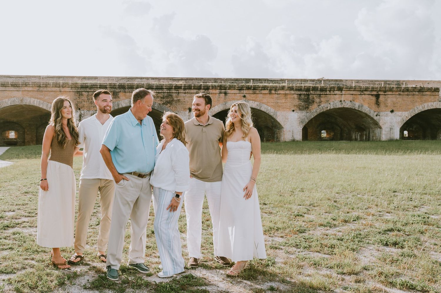 Happy family of six posing together outdoors near historic stone arches on a grassy field.