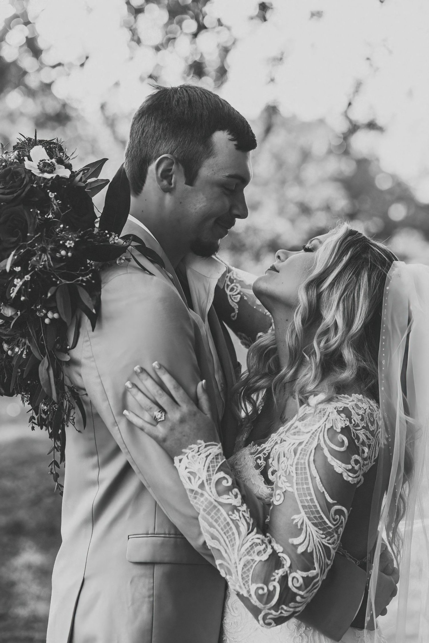 Black and white romantic portrait of bride and groom gazing at each other, bride holding bouquet.